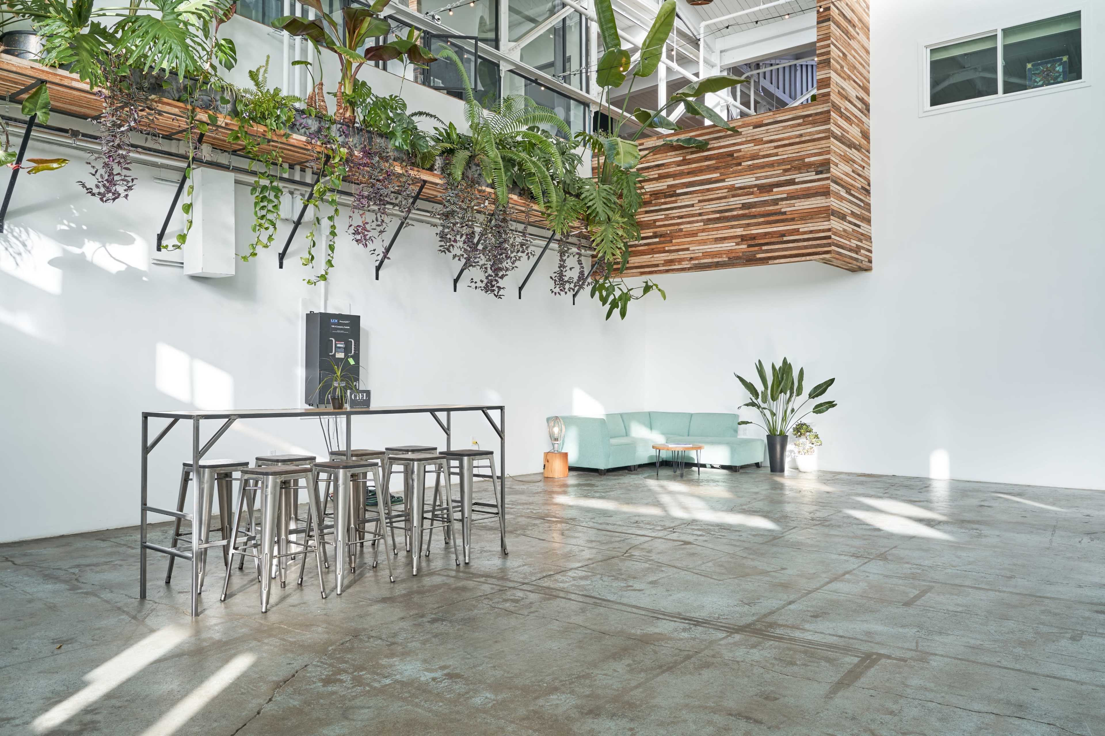 A spacious interior with a light-colored wall, a green sofa, a metal dining set, and hanging plants.