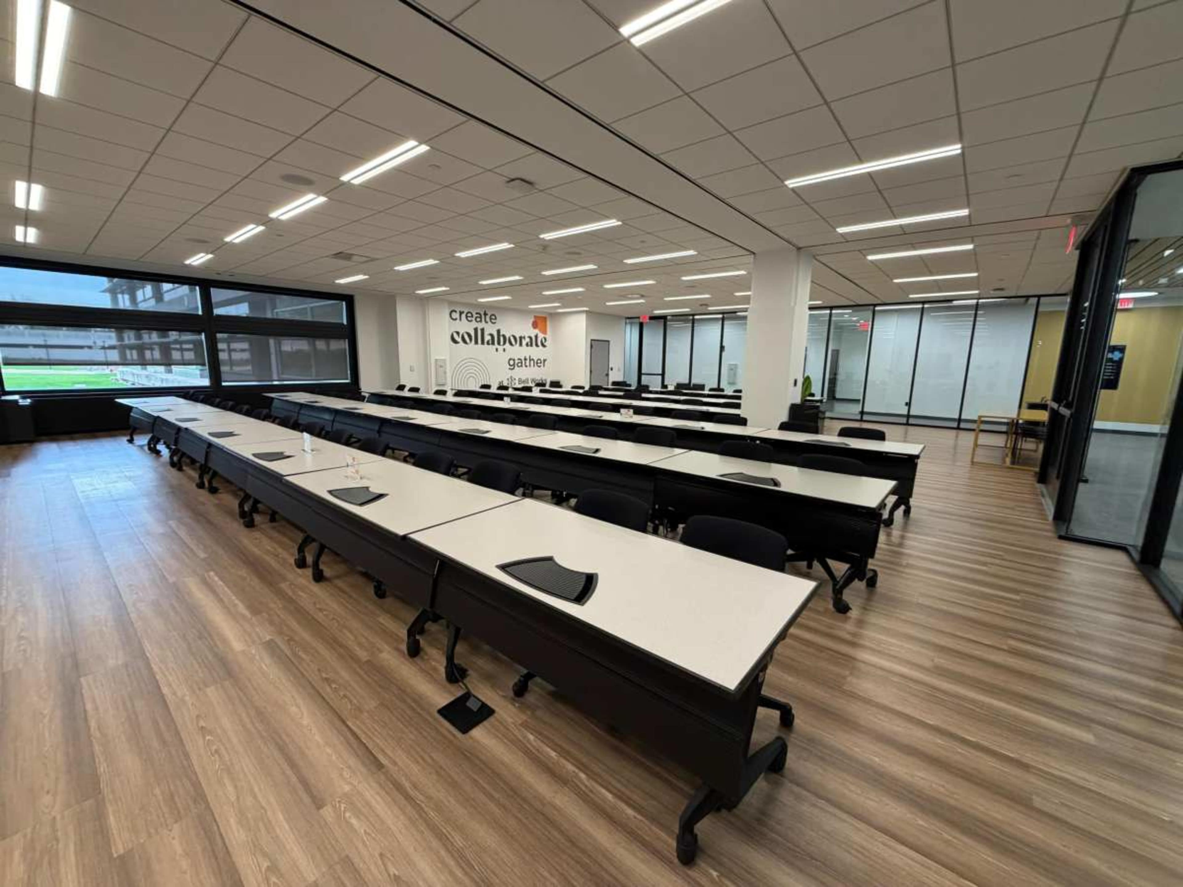 The image shows a modern classroom with rows of desks, a large window, and a wall featuring the words "create, collaborate, gather."