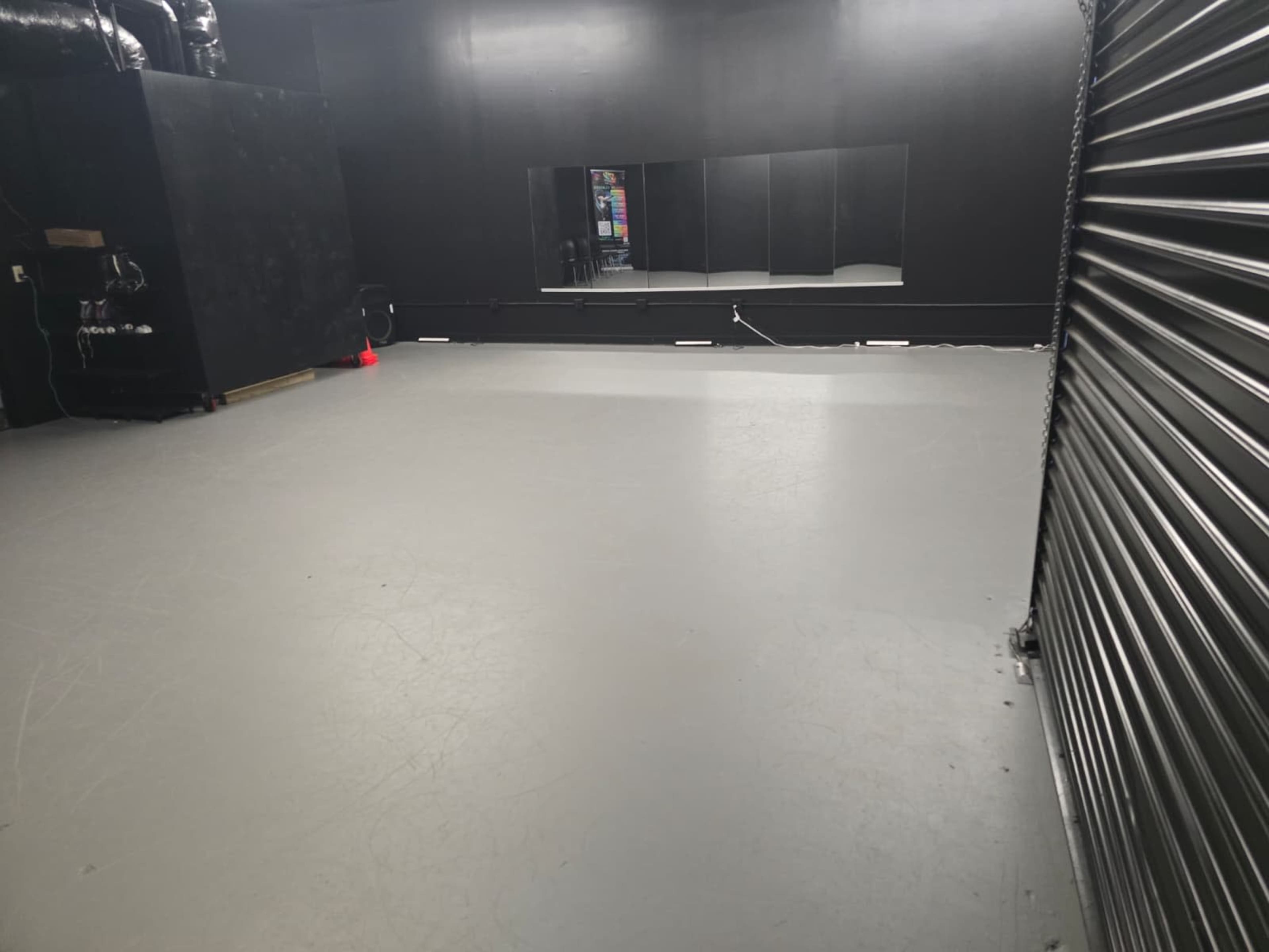 The image shows an empty room with a gray floor, black walls, and a mirror along one side.