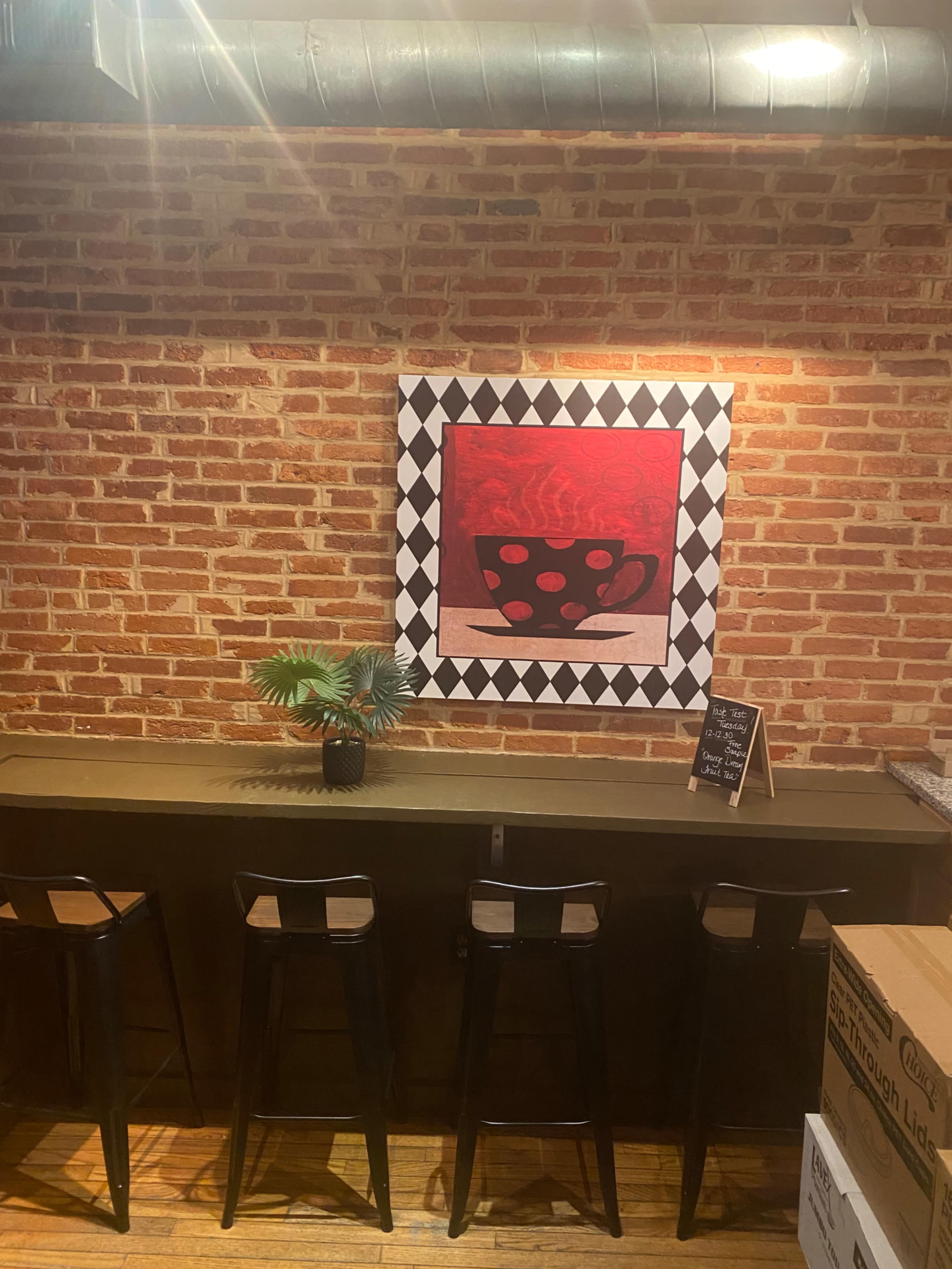 A bar area with four black stools, a brick wall, and an art piece featuring a cup on a red background.