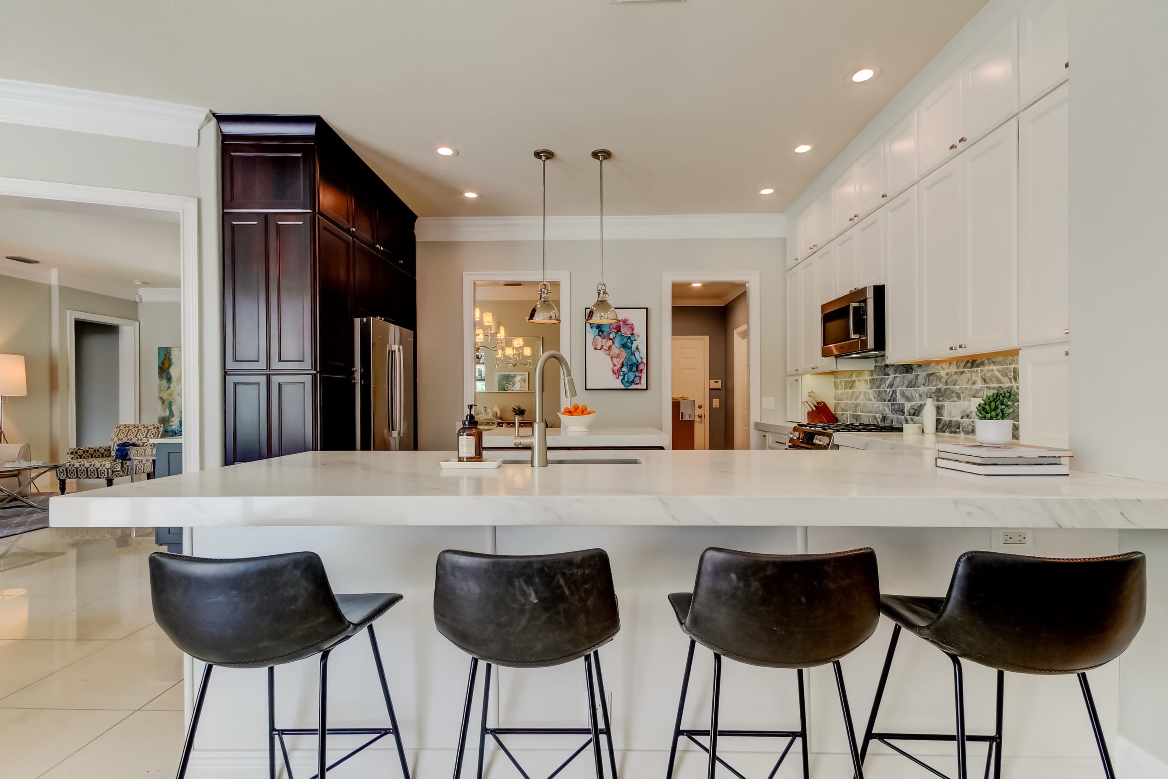 A modern kitchen features a large marble island with four black bar stools and dark cabinetry in the background.