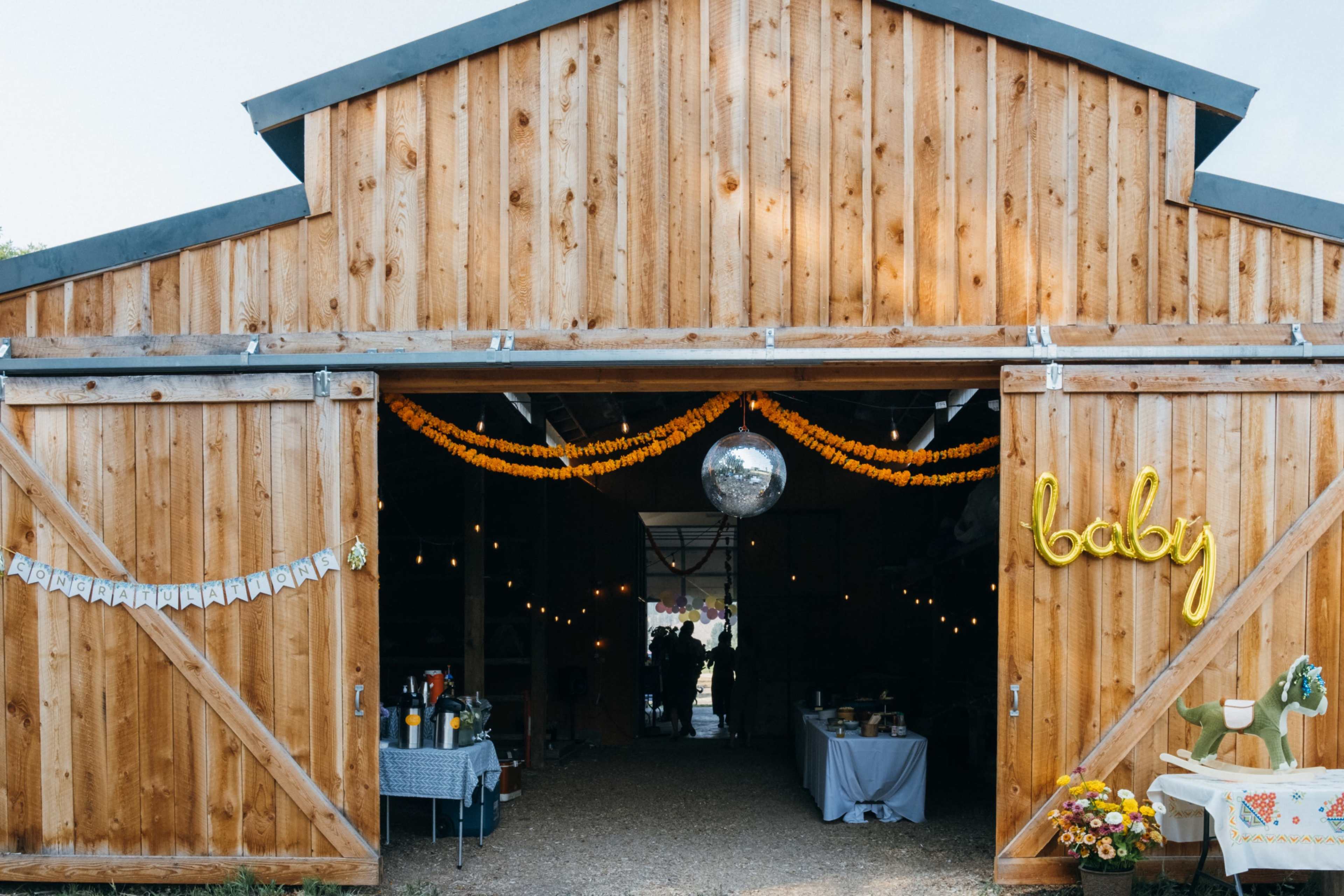 A wooden barn with an entrance adorned with yellow decorations and a disco ball hangs inside.