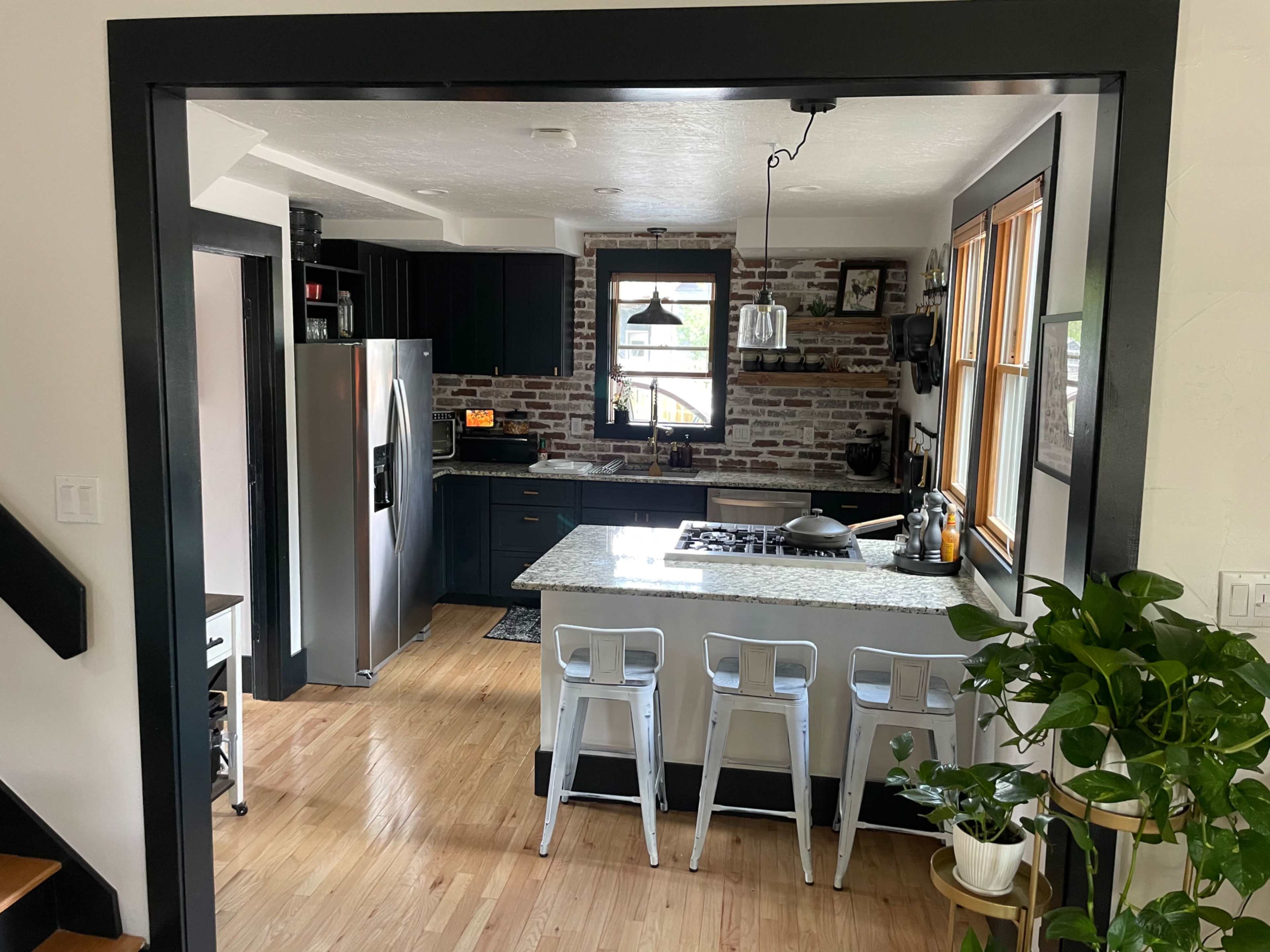 A modern kitchen with dark cabinetry, a granite countertop, and a view of a dining area through a framed opening.