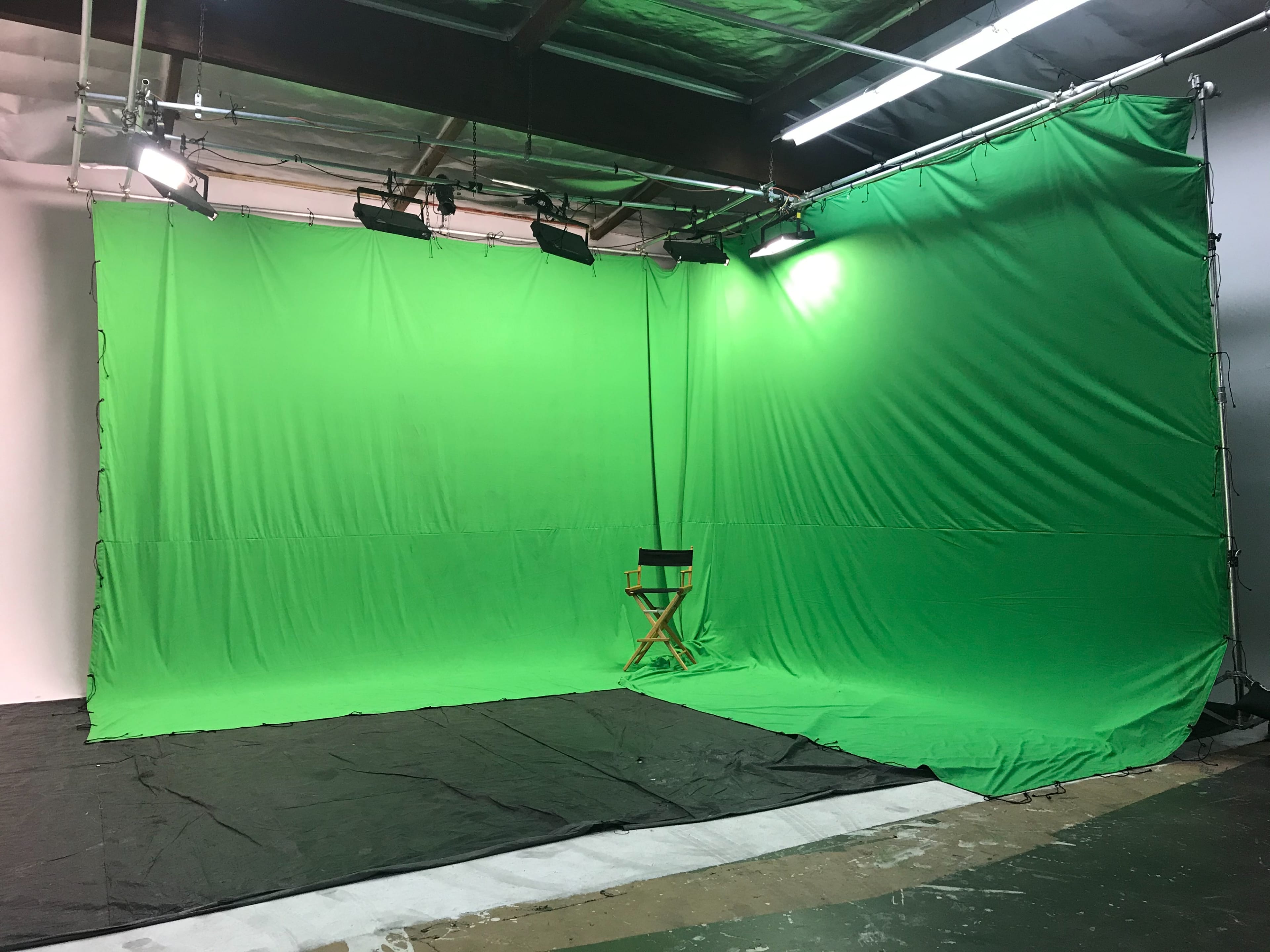 A green screen setup in a studio, with lights positioned above and a director's chair placed in front.