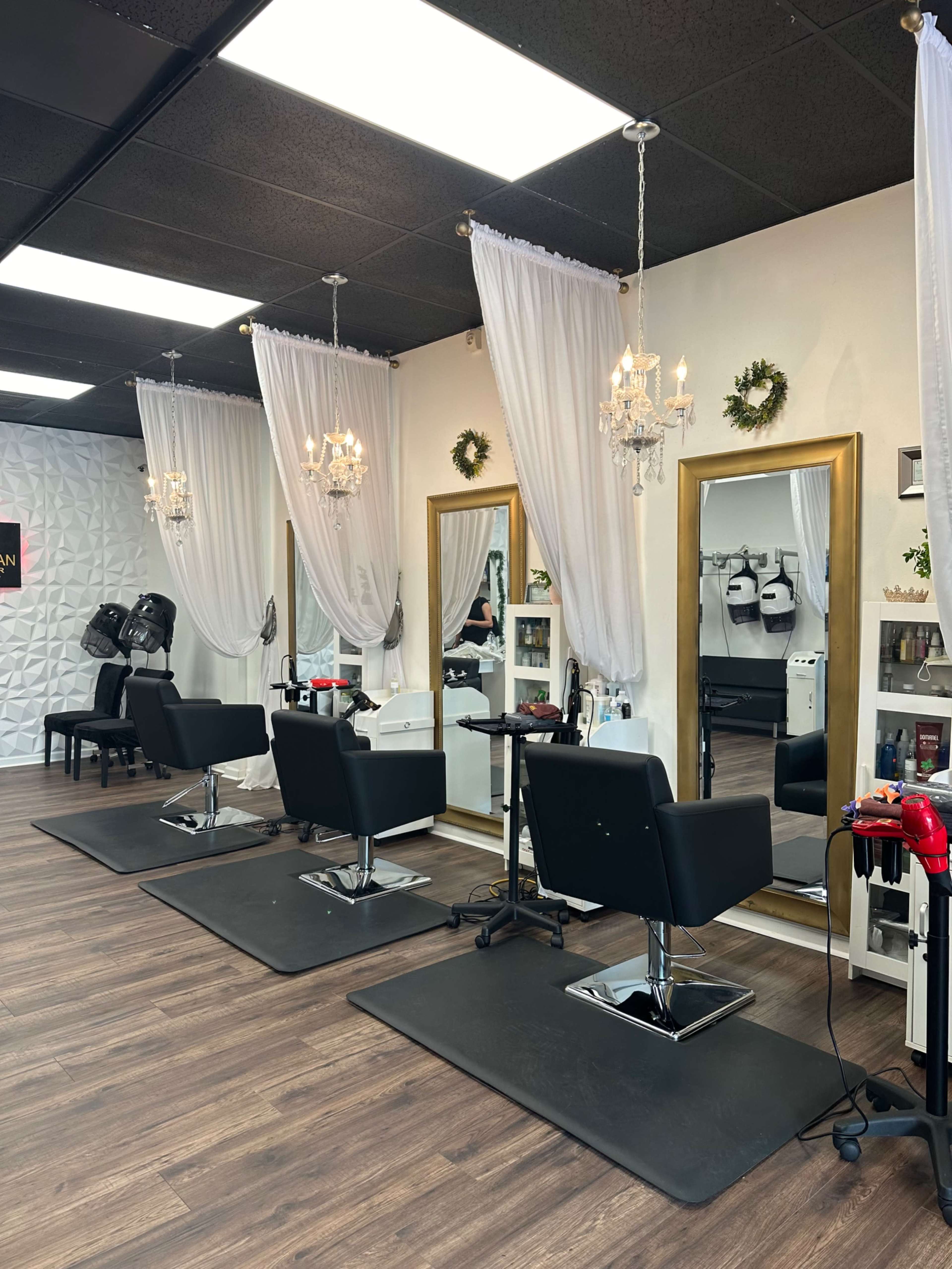 The image depicts a modern hair salon featuring three styled salon stations with large mirrors, elegant drapes, and decorative chandeliers.