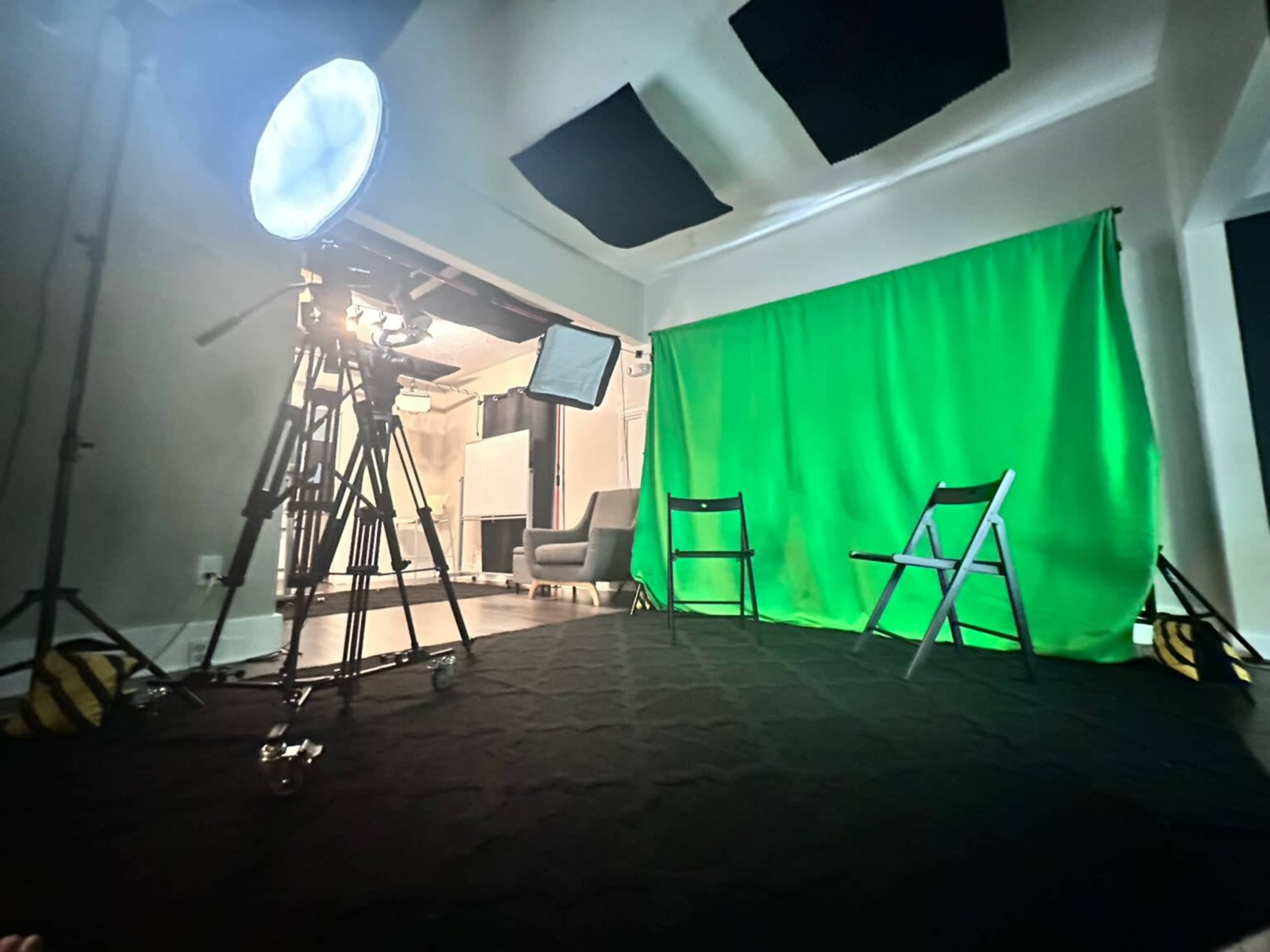 A video production setup with a green screen, two chairs, and lighting equipment in a studio environment.