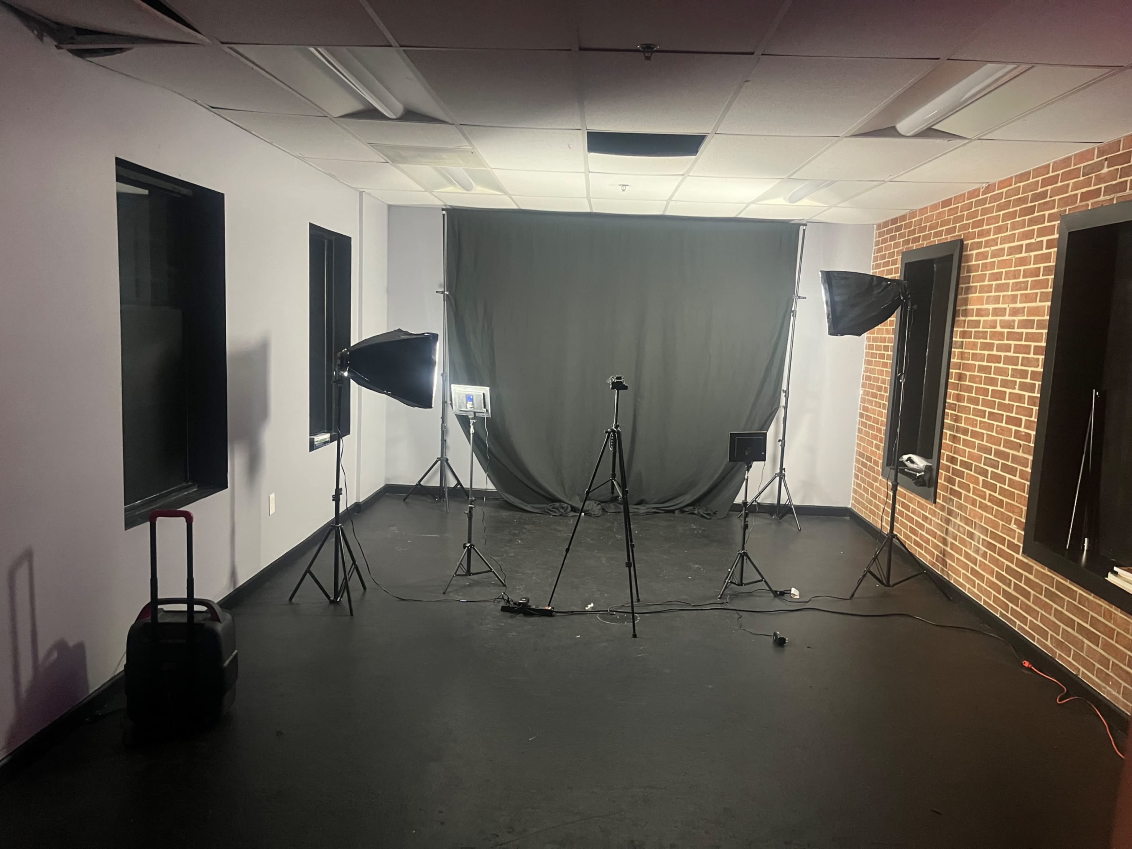 A dimly lit studio setup with a gray backdrop, two softbox lights on stands, and a camera tripod positioned in front.