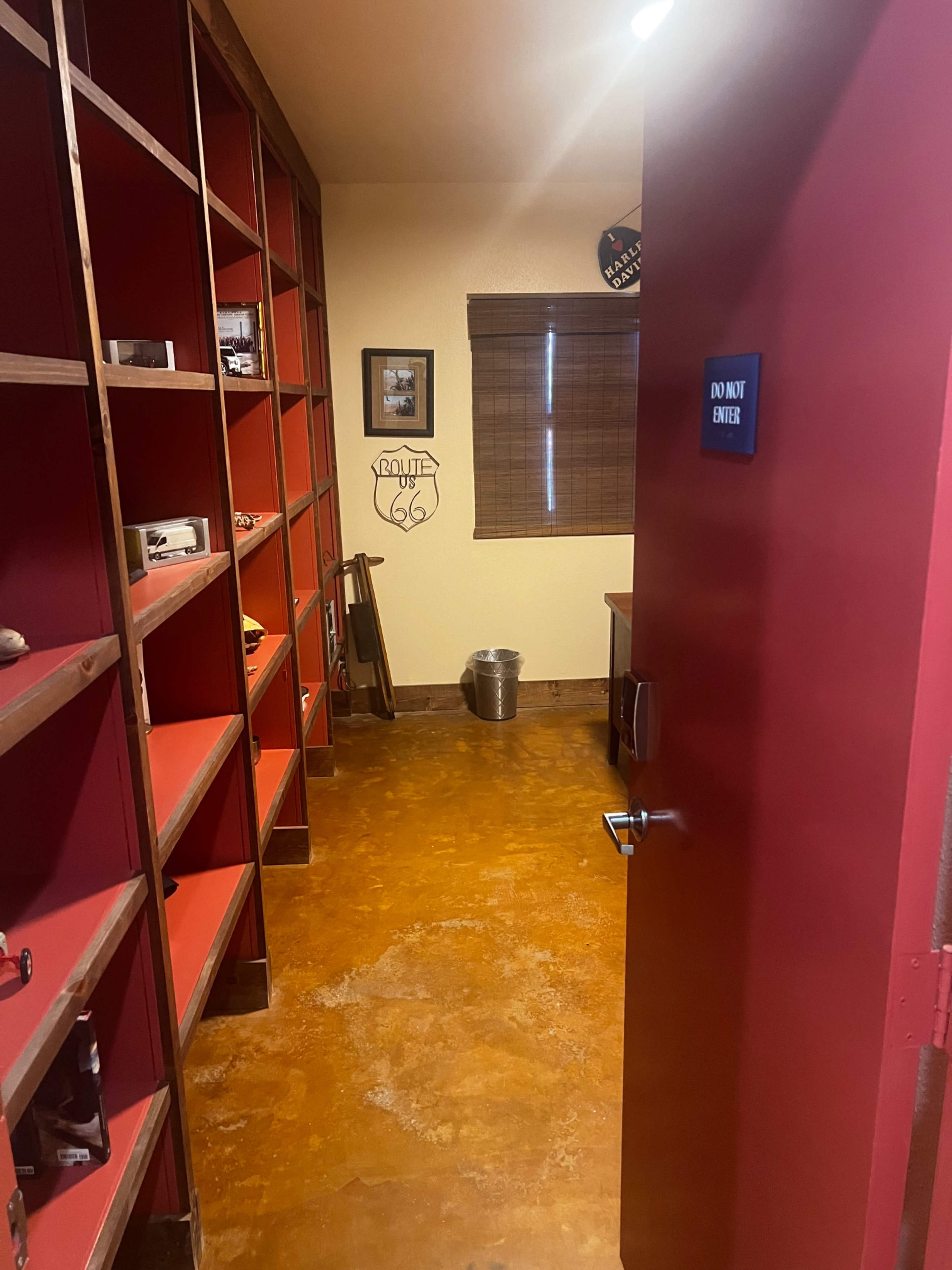 The image shows a room with red shelves lined with various items and a desk, visible through an open door.