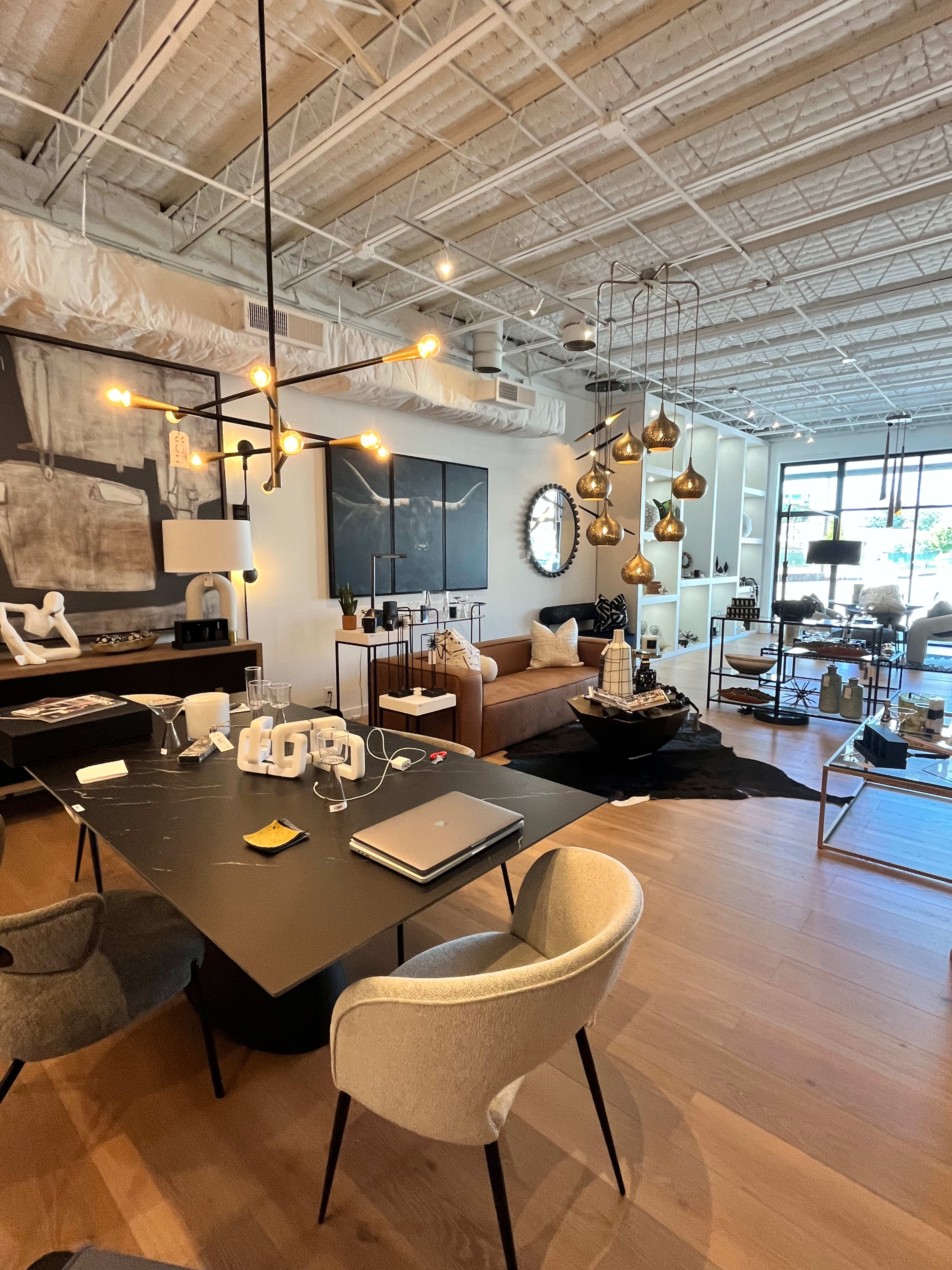 A modern, open-concept office space with a dining table, chairs, a couch, decorative lighting fixtures, and various decor items on display.