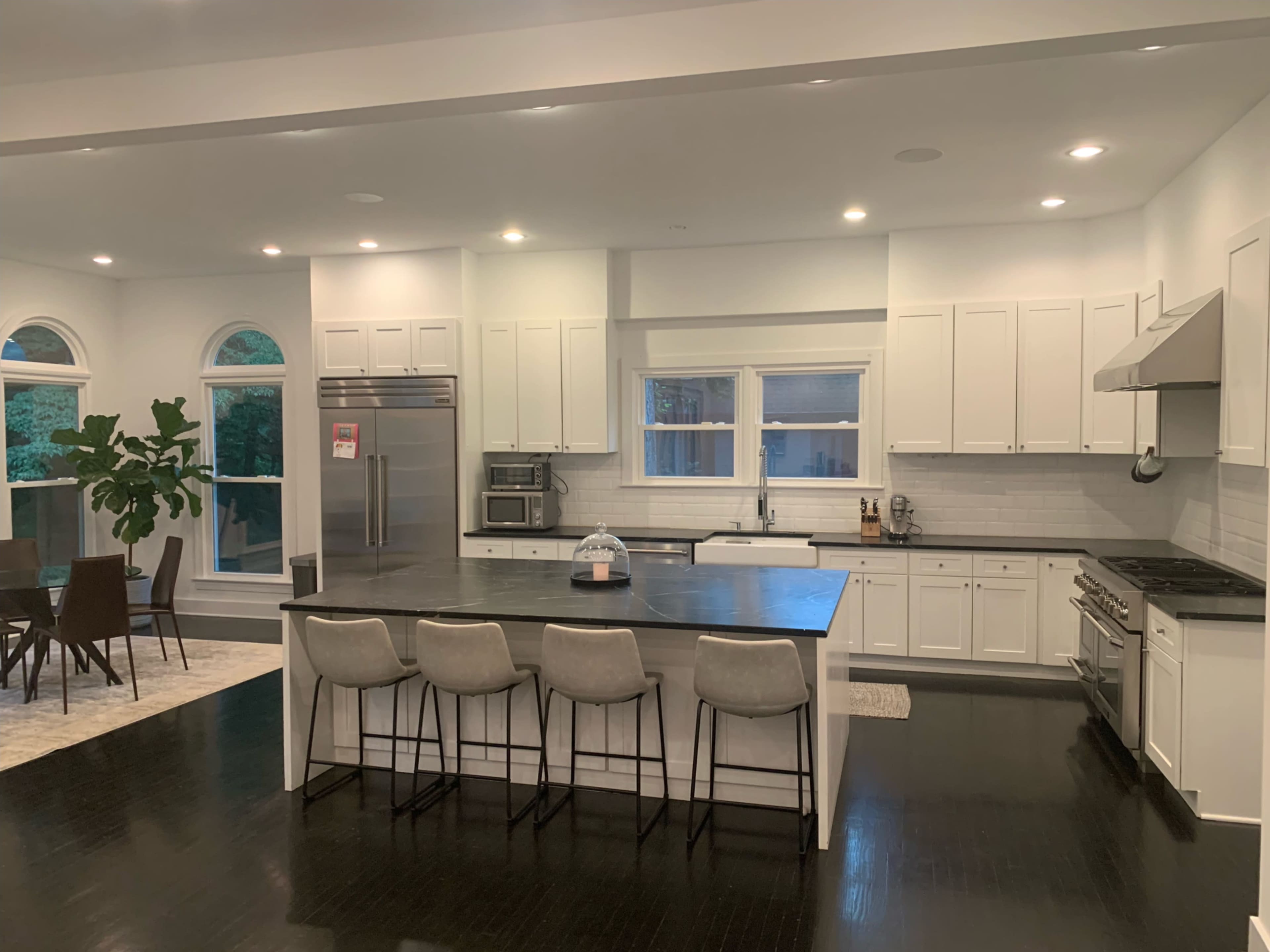 A modern kitchen features a large island with four stools, stainless steel appliances, and a view of a dining area with a table and chairs.