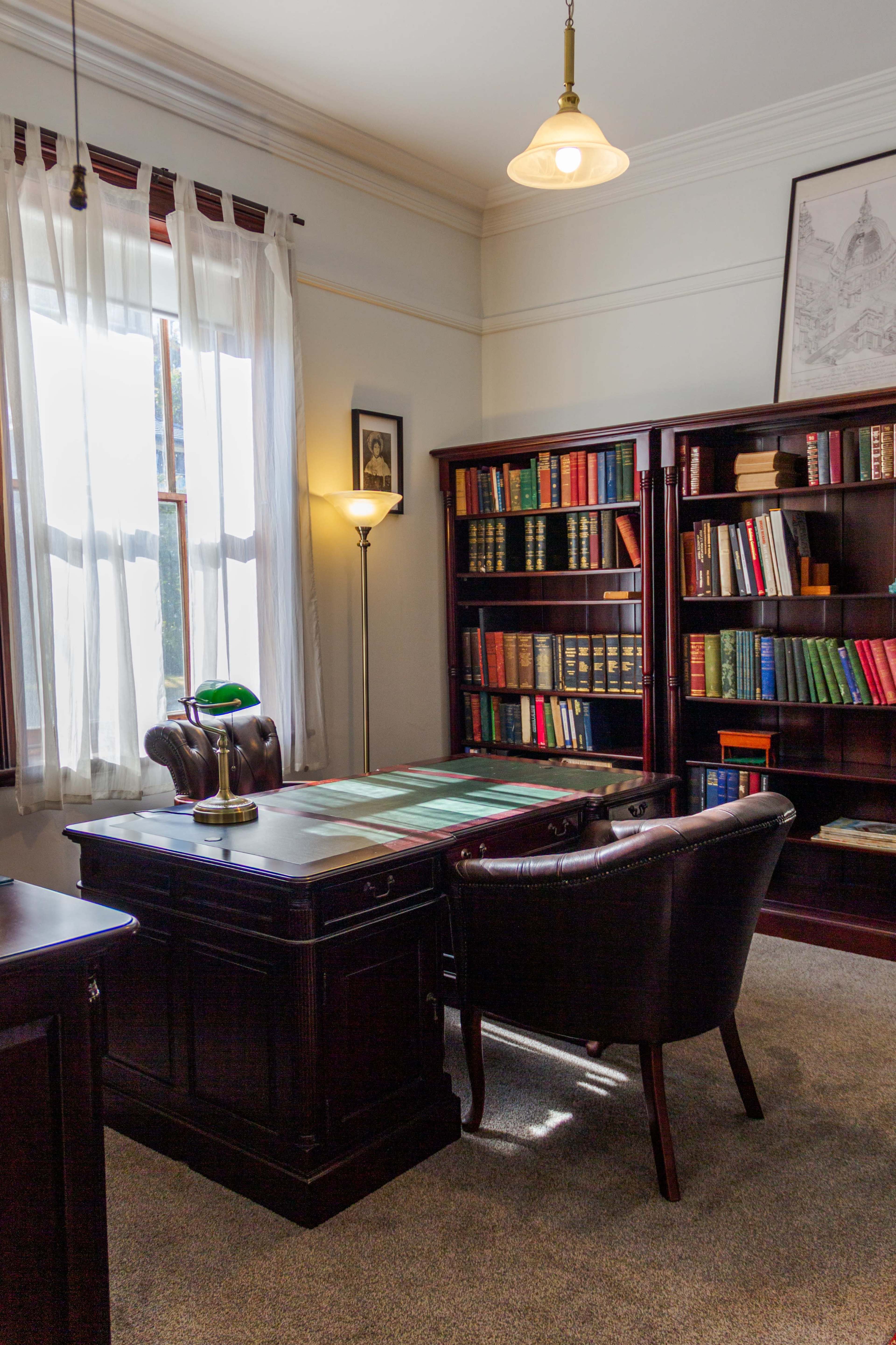 The image depicts a well-furnished office with a desk, a reading lamp, and bookshelves filled with books.
