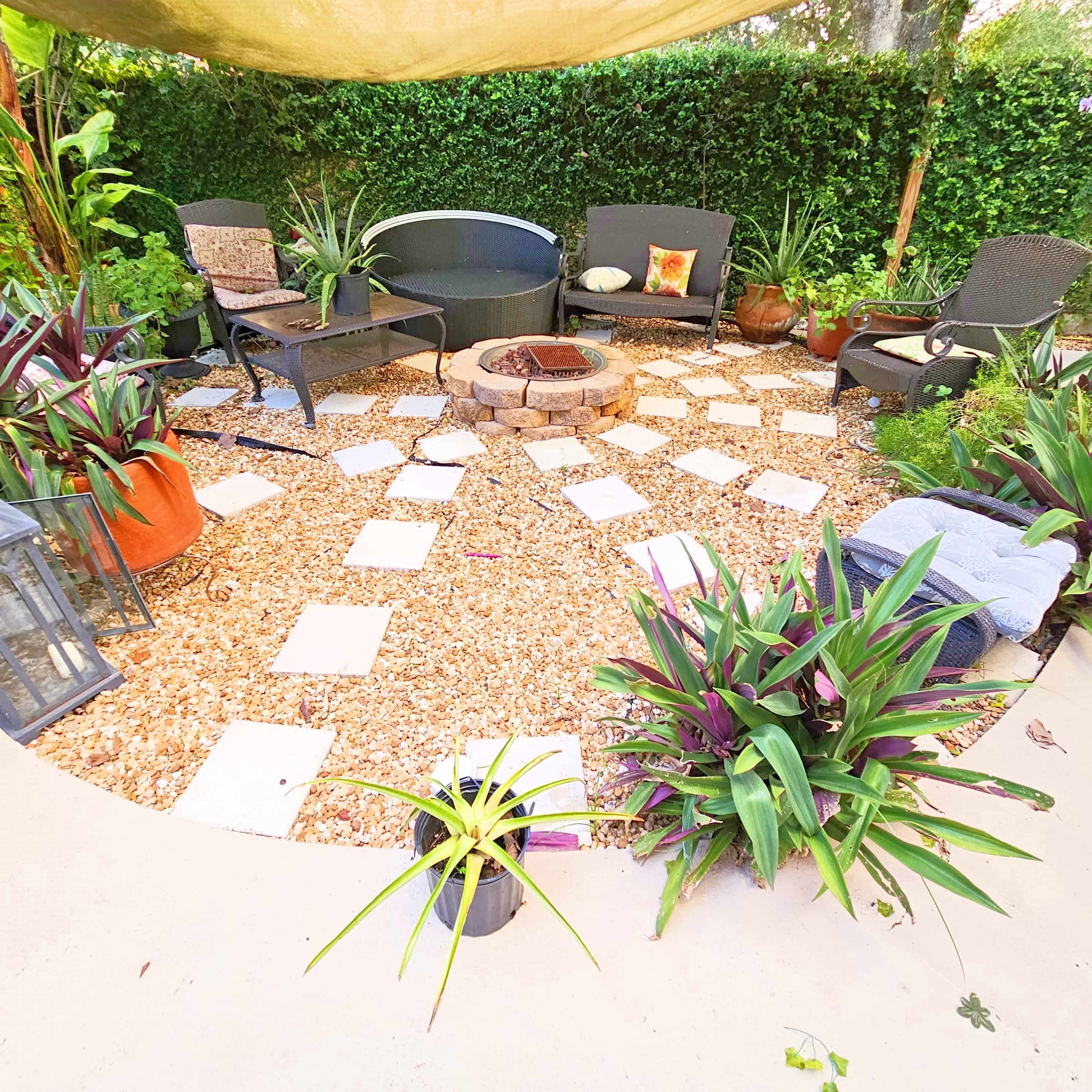 A circular outdoor seating area with stone pathways leading to a fire pit, surrounded by various potted plants.