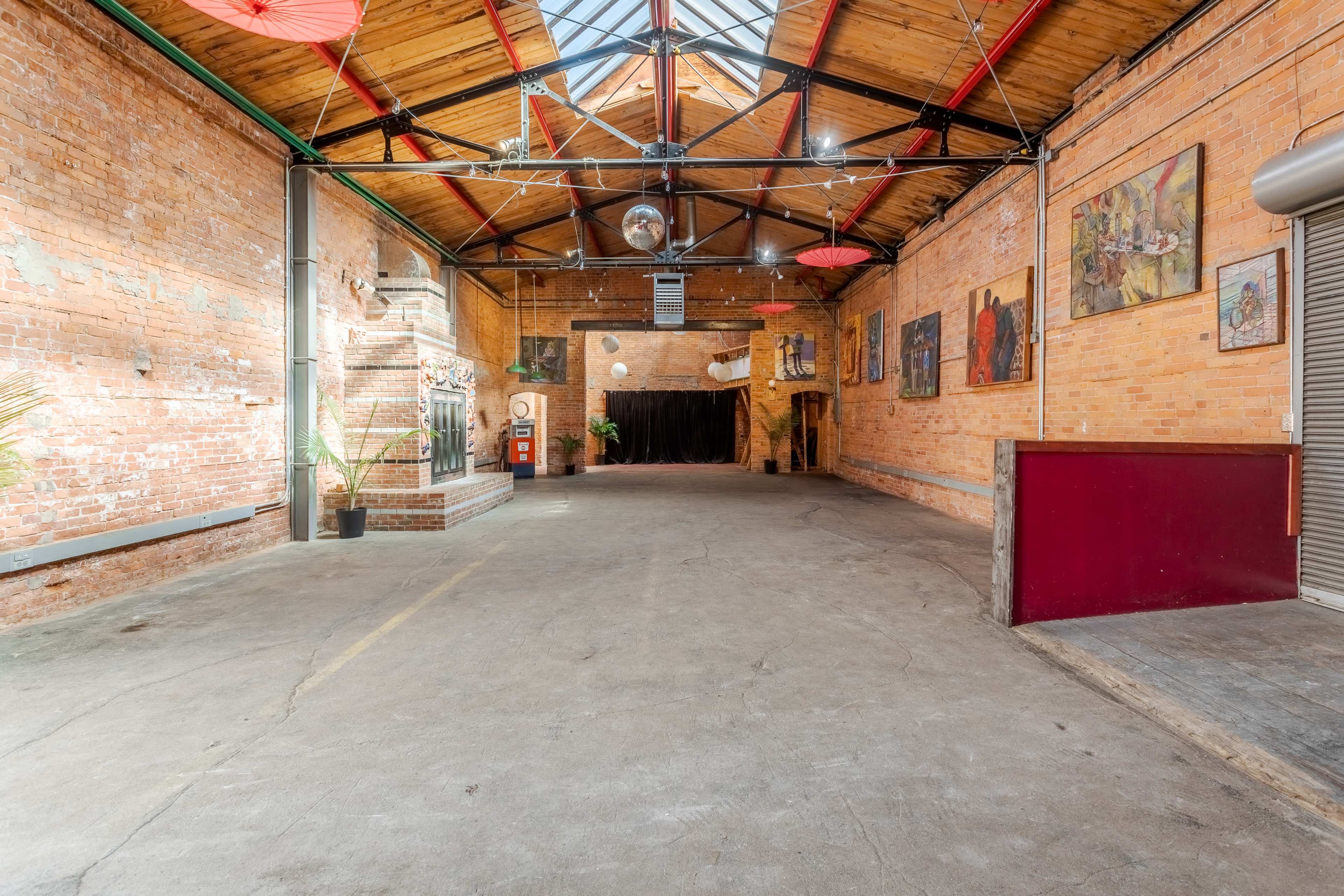 A spacious, well-lit industrial hall with exposed brick walls, a wooden ceiling, and various artworks displayed on the walls.