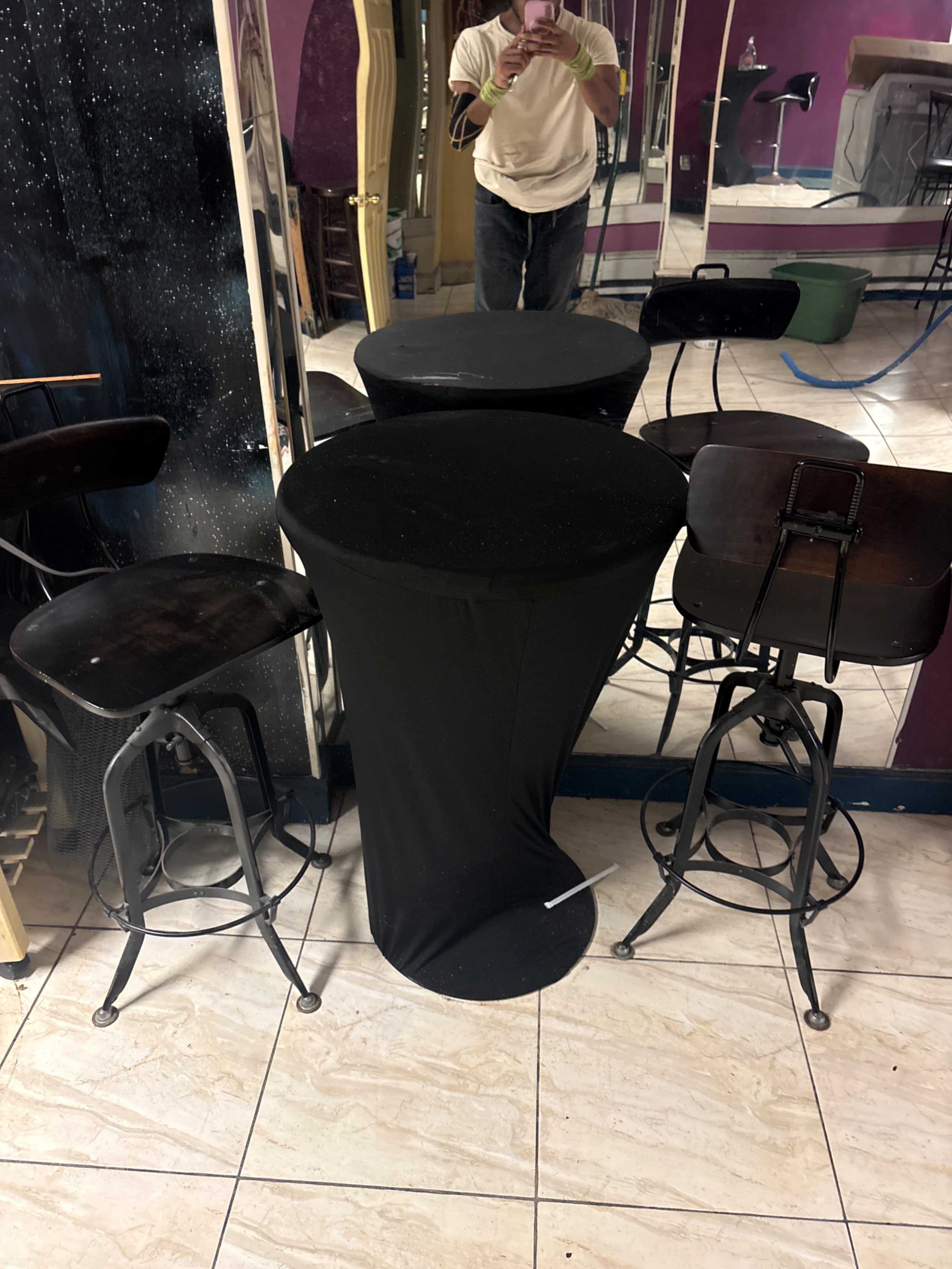 The image shows a small black table surrounded by two wooden bar stools in a room with purple walls and mirrors.