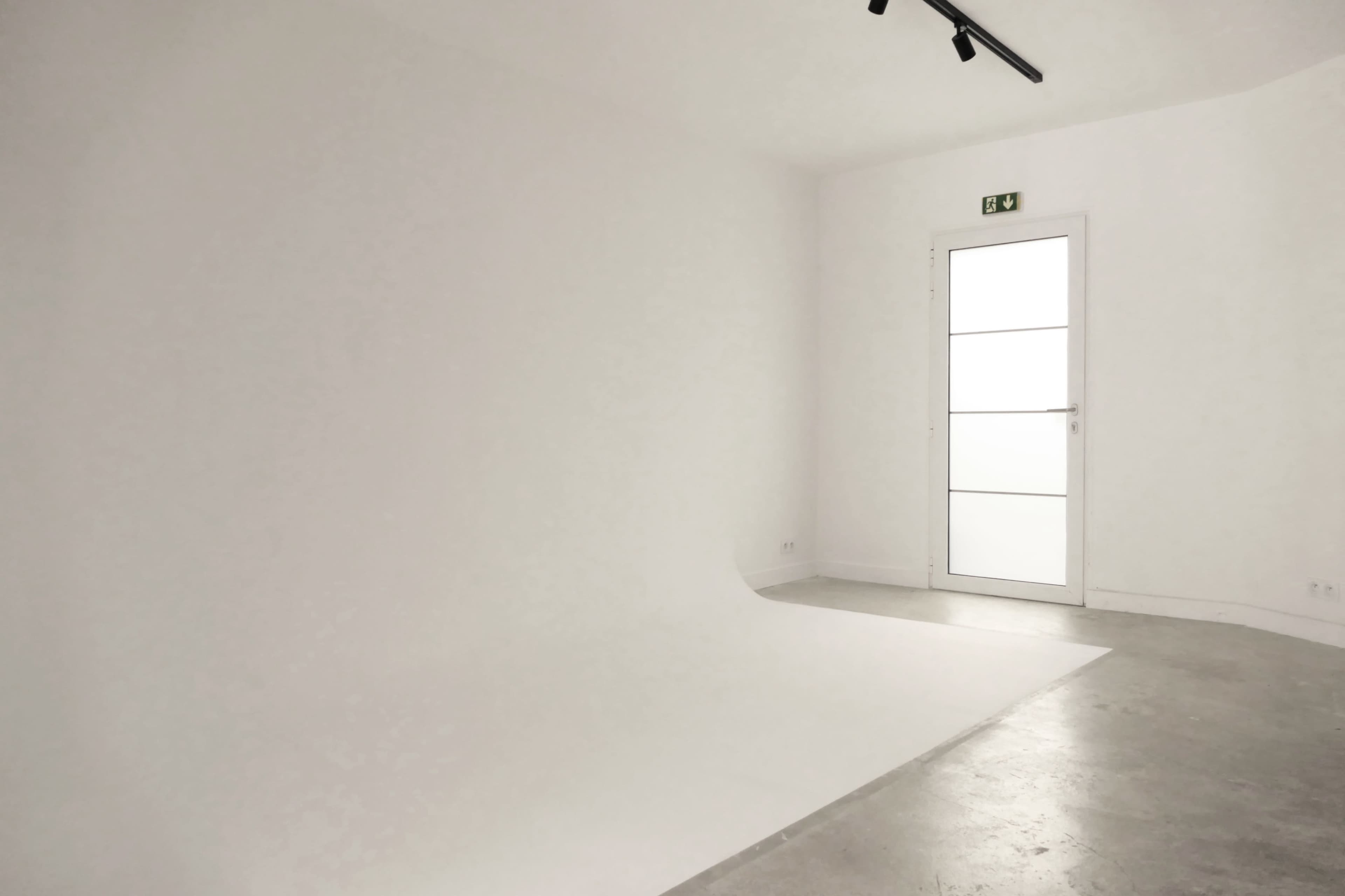 A minimalist room with a white backdrop, concrete flooring, and a glass door.