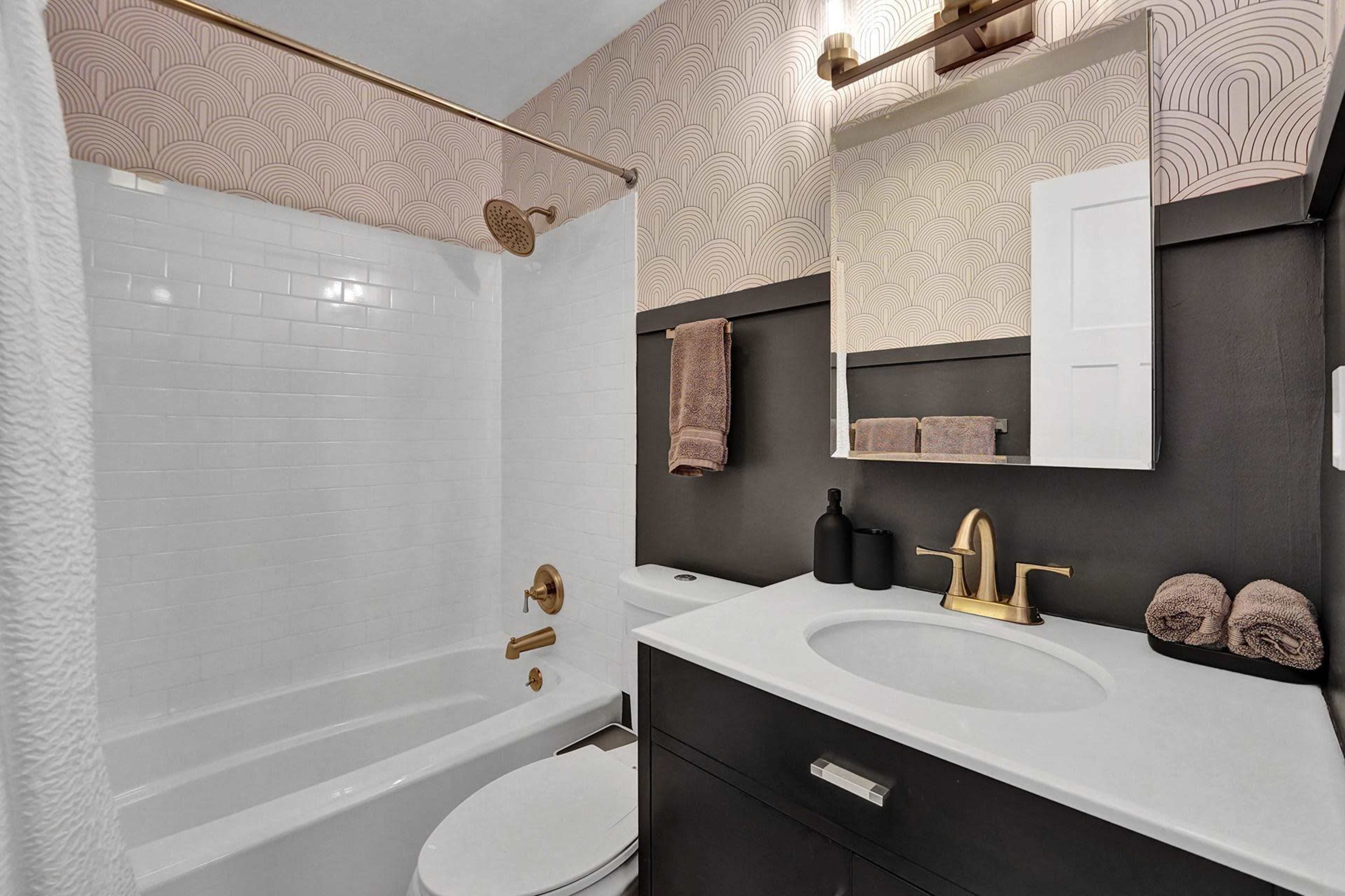 The bathroom features a white tiled shower area, a gold faucet, and a modern black vanity with a round mirror.