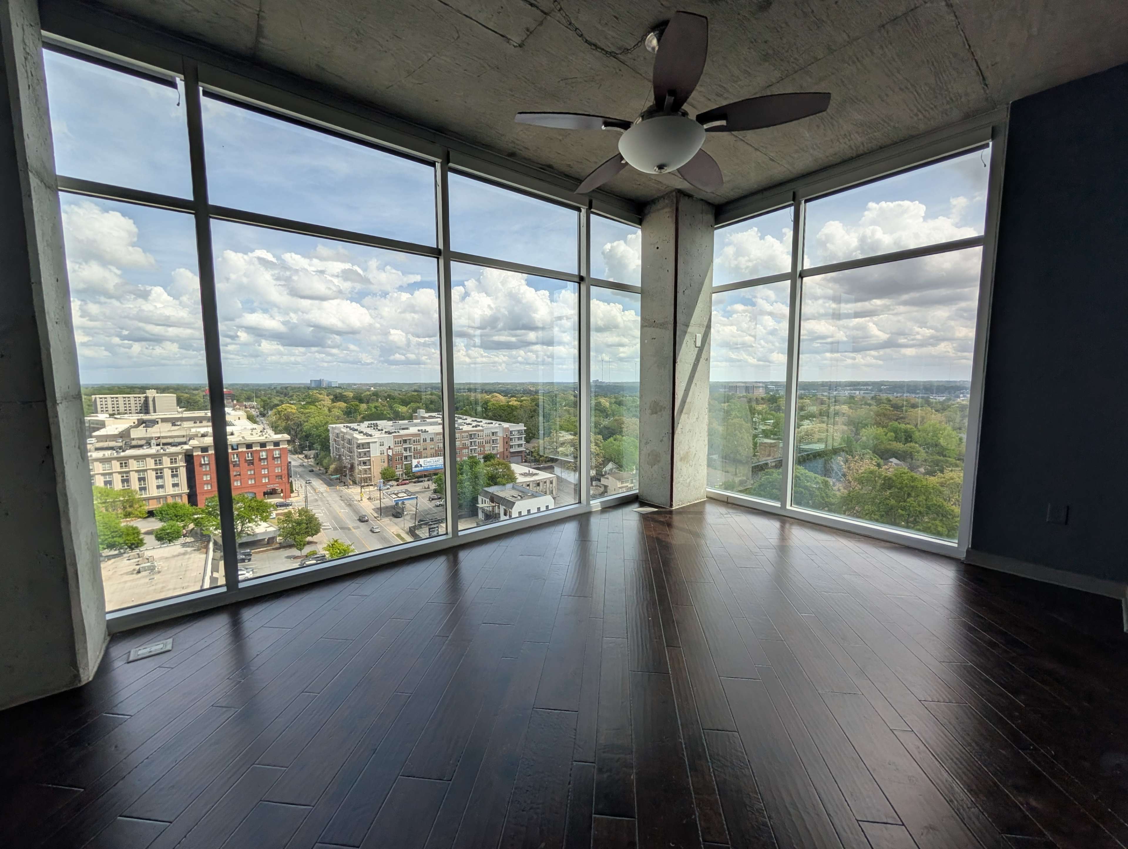 A spacious room with large windows offers a view of a city skyline and blue sky filled with clouds.