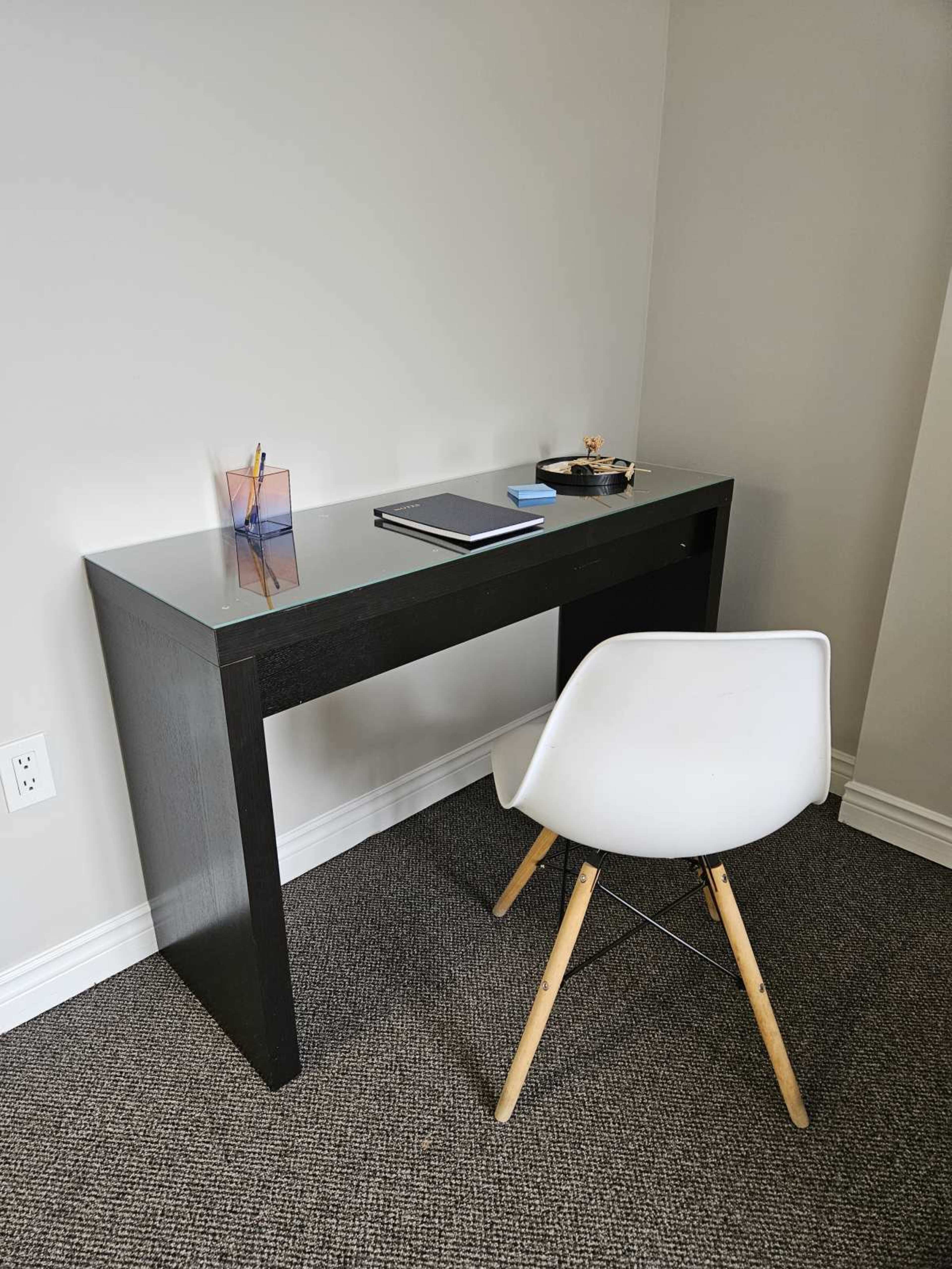 A minimalist desk with a dark finish is positioned against a light gray wall, accompanied by a white chair and various office supplies.