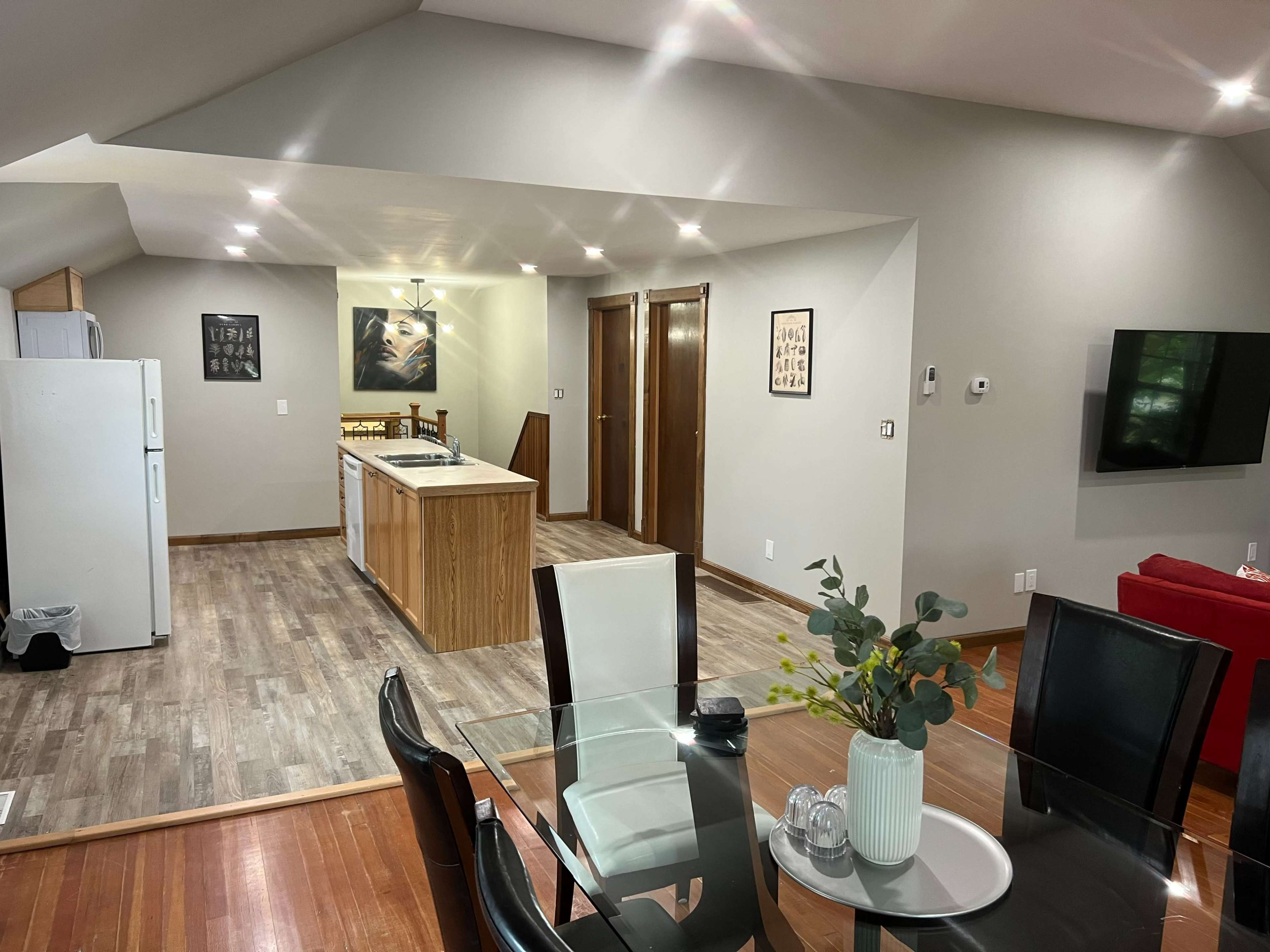The image shows a modern kitchen and dining area with a table, chairs, and an island, featuring wood and neutral-colored walls and flooring.