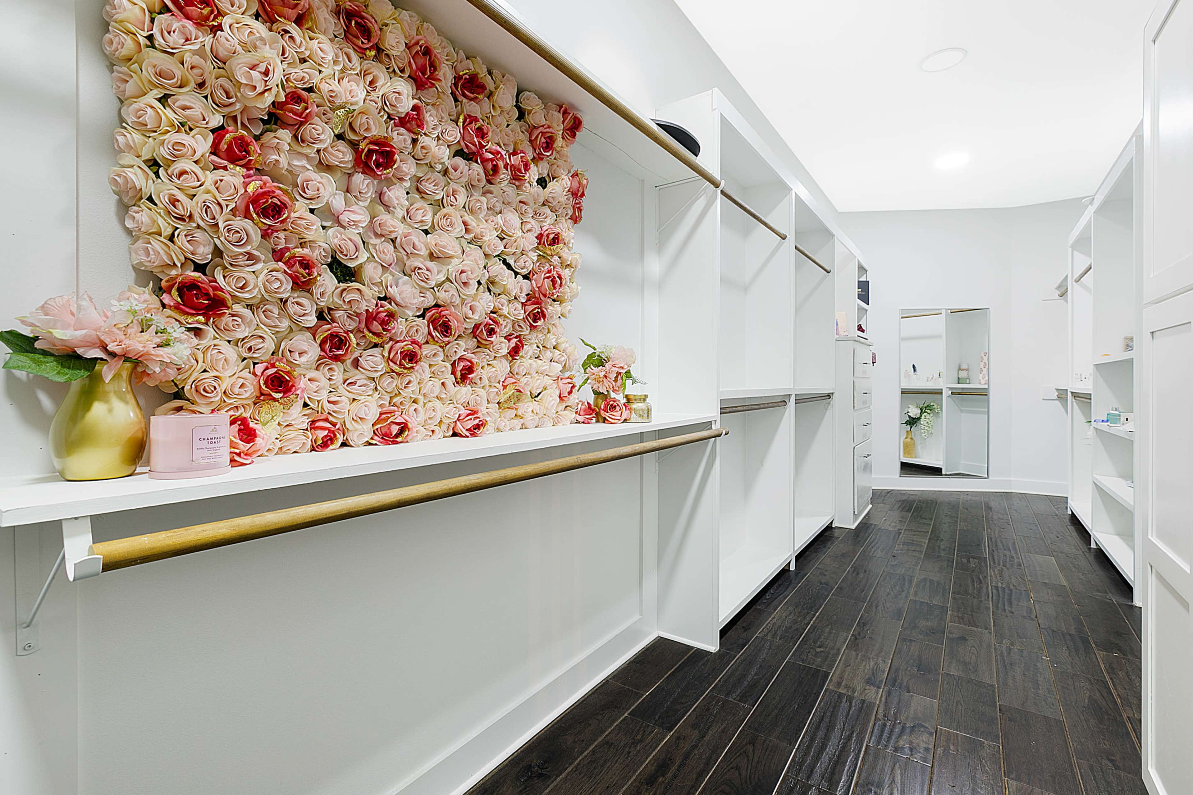 A spacious room features white shelves and cabinetry alongside a decorative wall made of pink and red artificial roses.