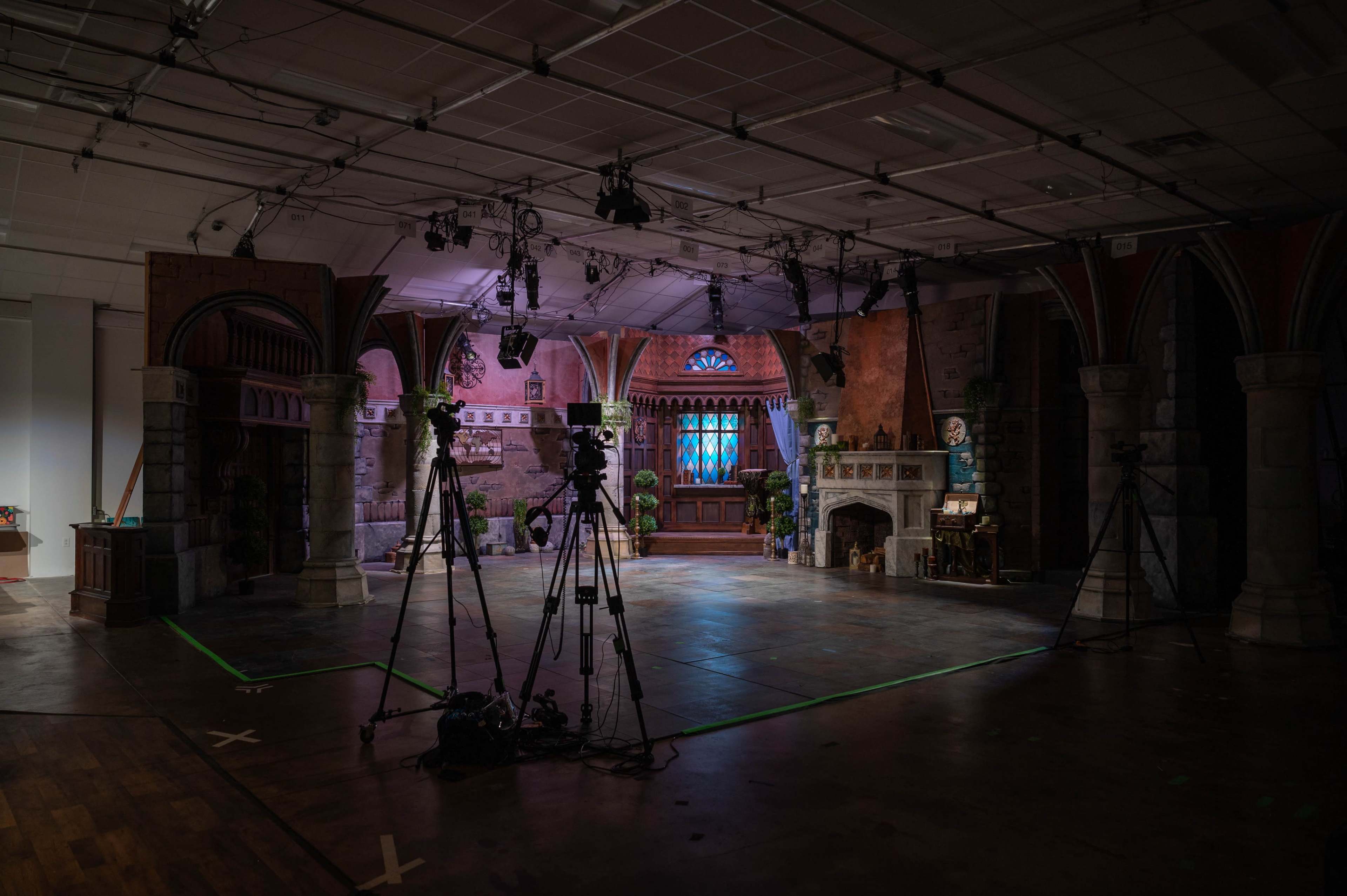 A television studio set features a castle-like interior with cameras positioned around a central stage.