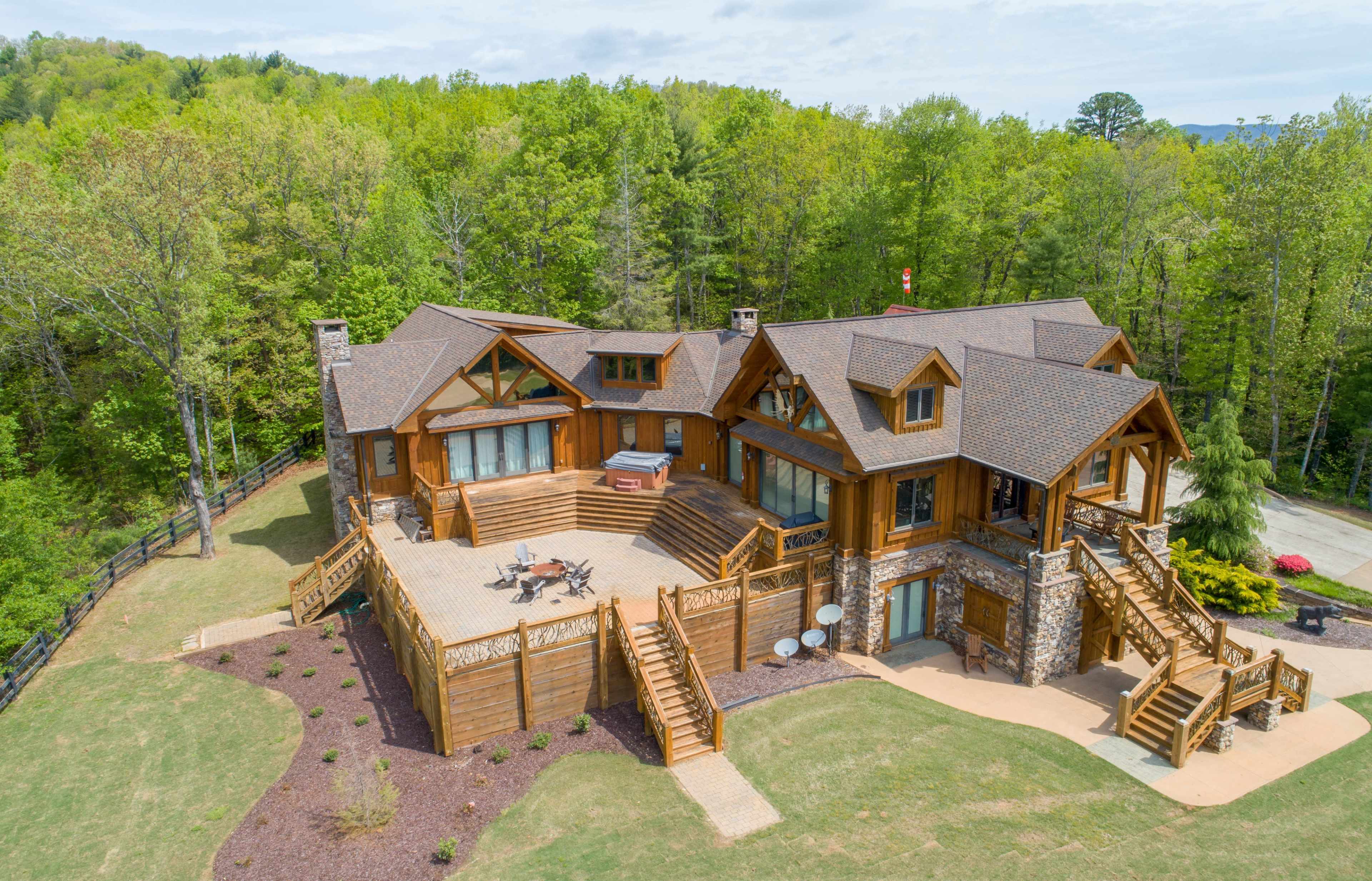 A large, multi-level wooden house surrounded by trees, featuring a spacious deck and a landscaped yard.