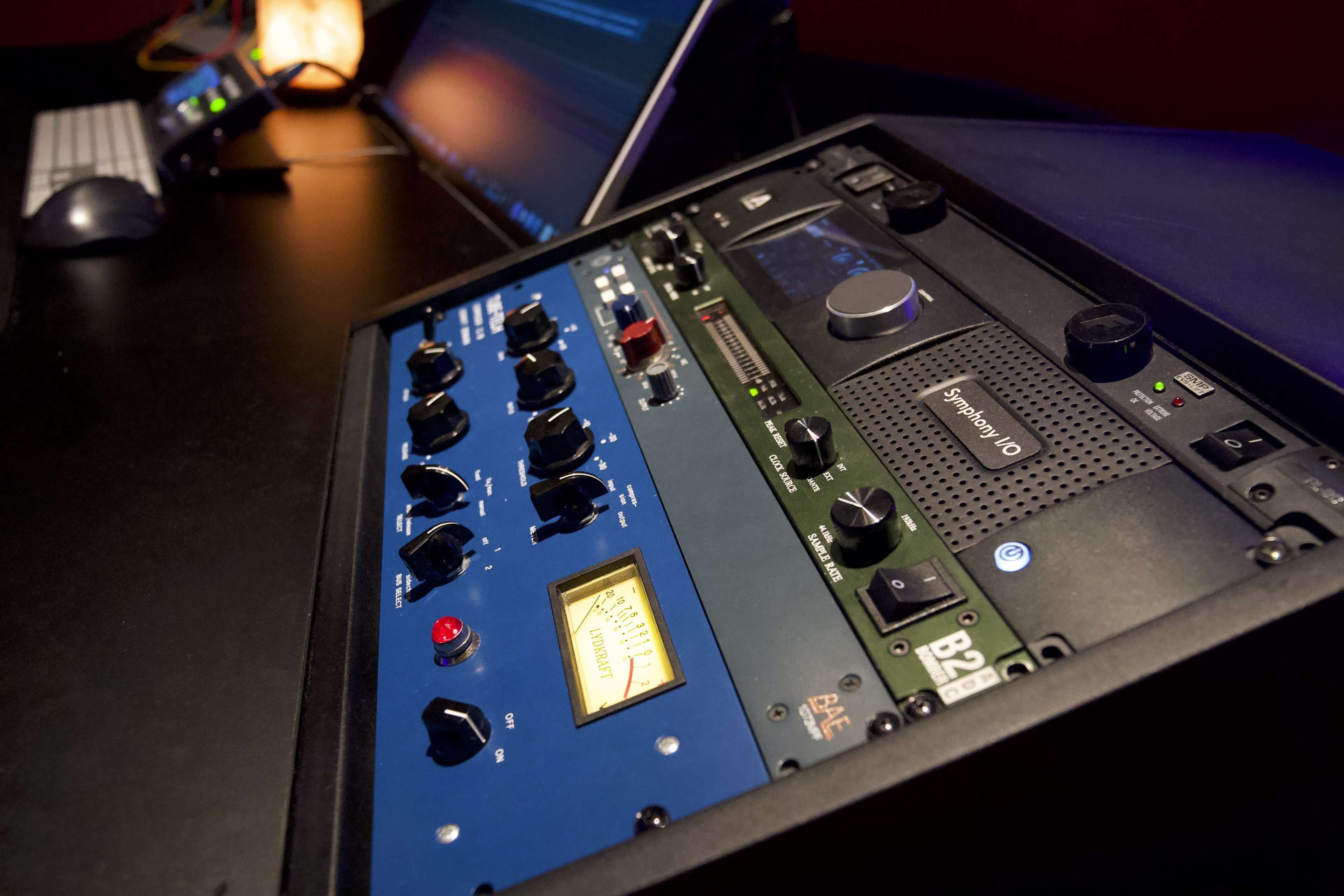 A close-up of audio equipment, featuring various knobs, buttons, and meters on a black and blue rack mounted device in a studio setting.
