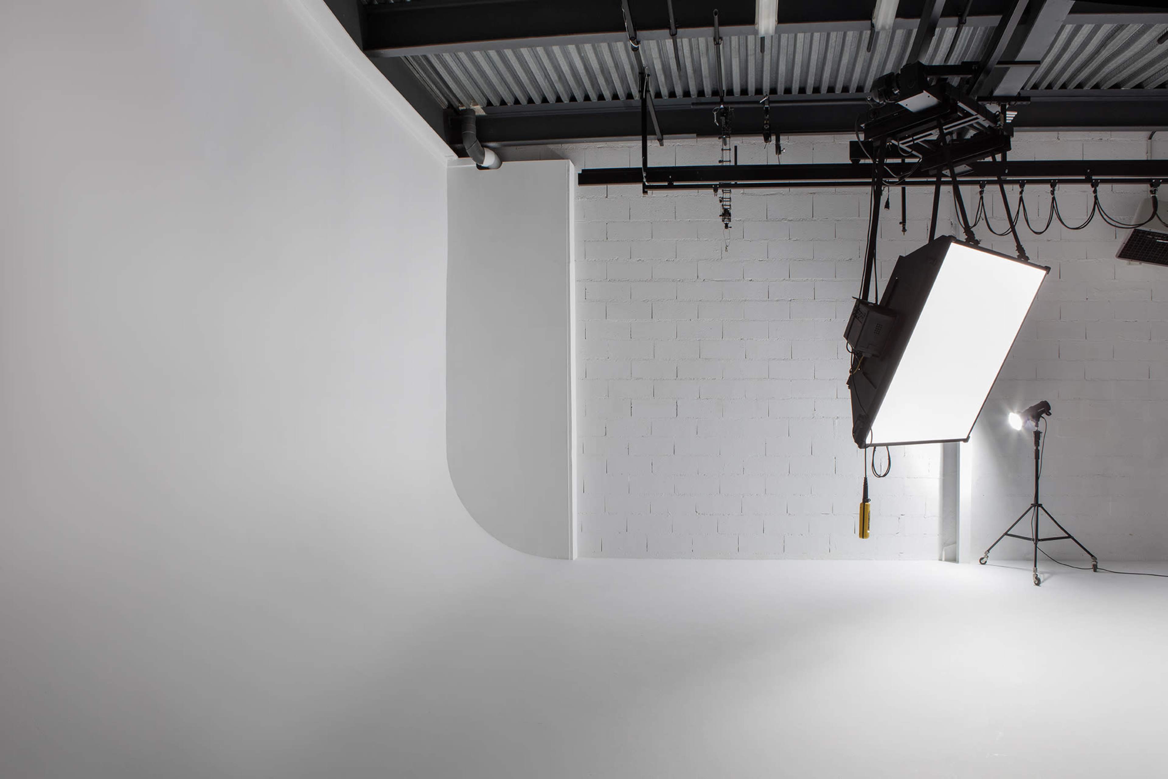 A minimalistic photography studio with a curved white backdrop and overhead lighting equipment.