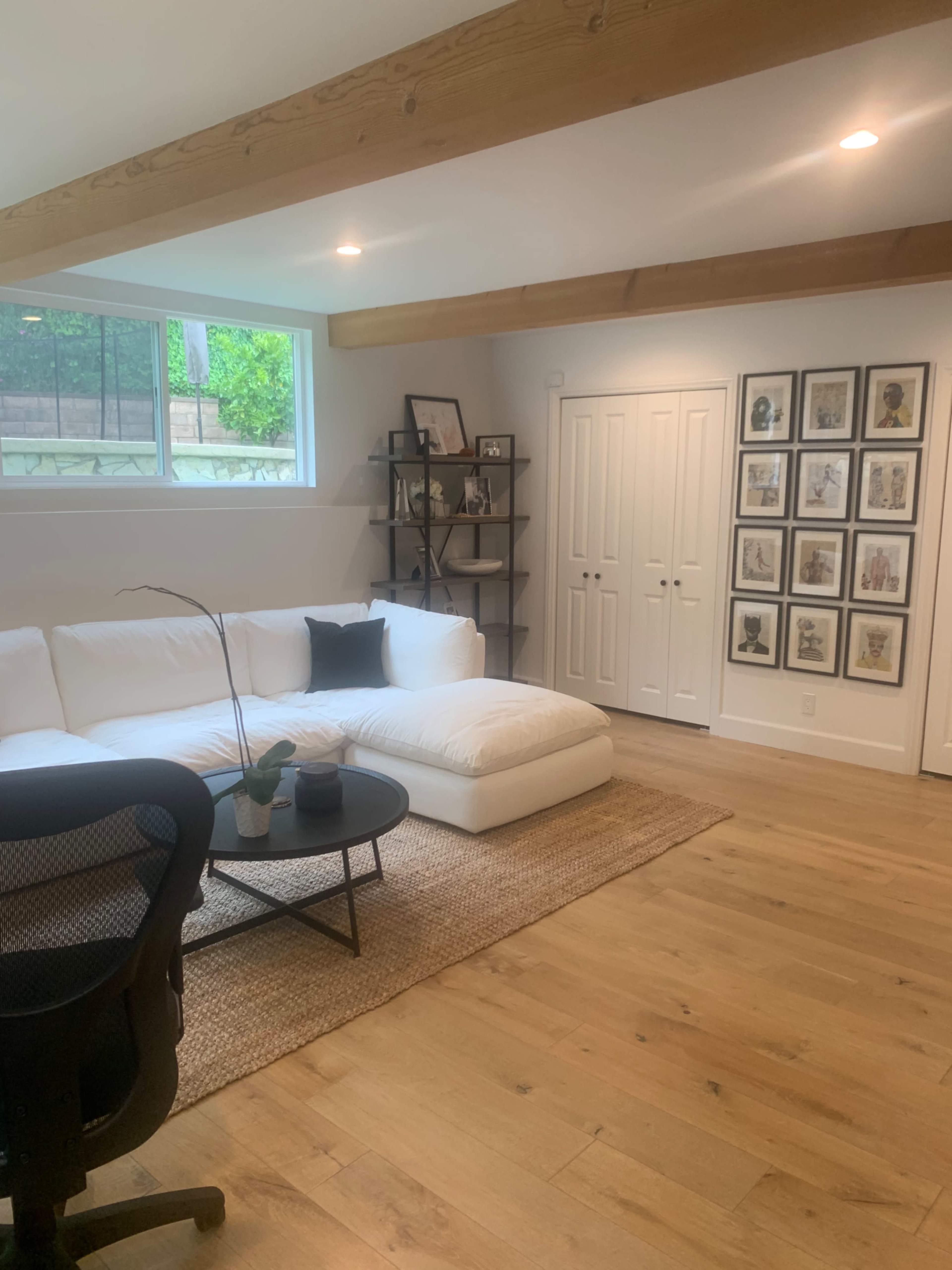 A modern living room features a large white sectional sofa, a round black coffee table, and a gallery wall of framed pictures alongside a shelving unit.
