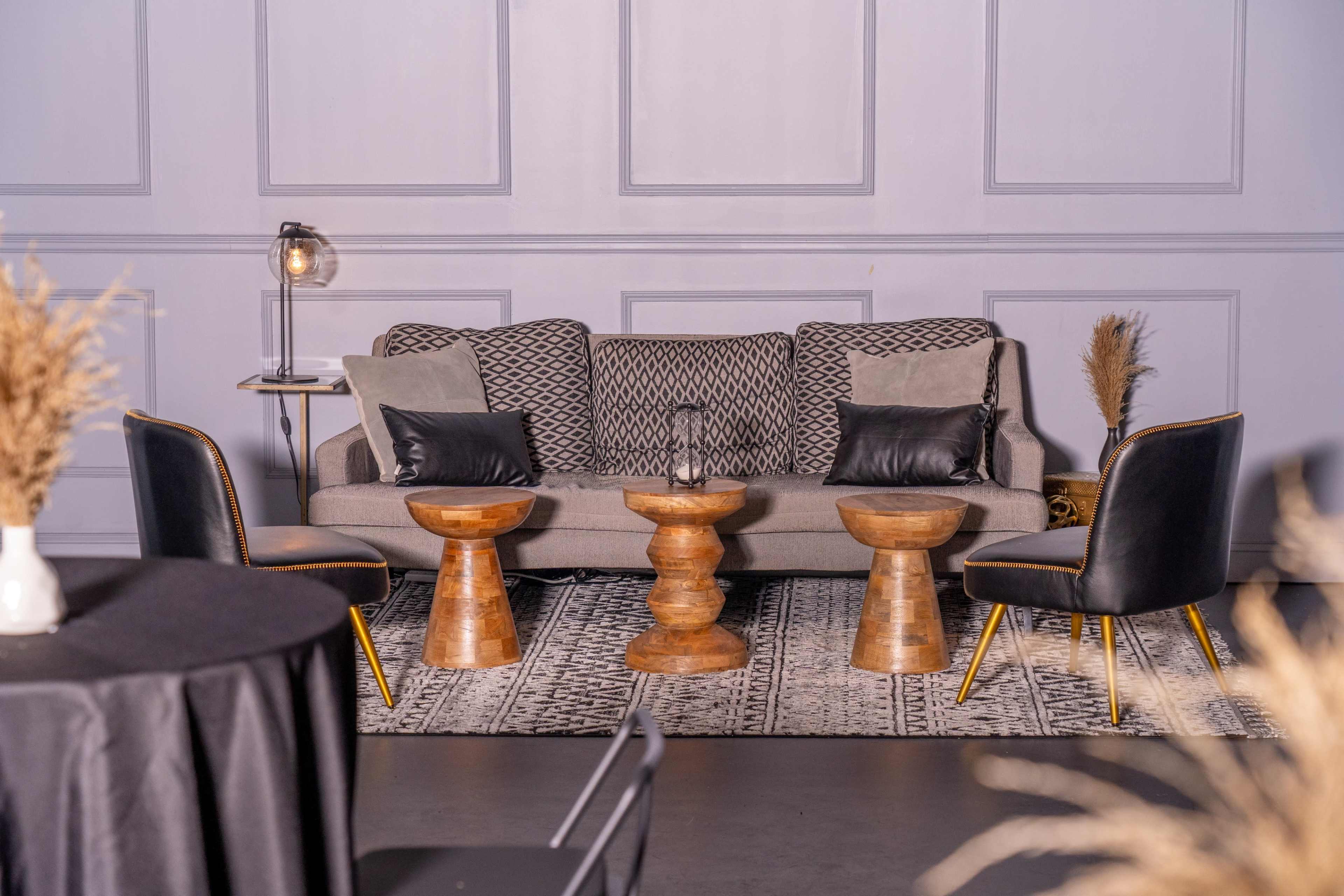 A modern living room setup featuring a patterned sofa, two wooden side tables, and black chairs arranged around a stylish rug.