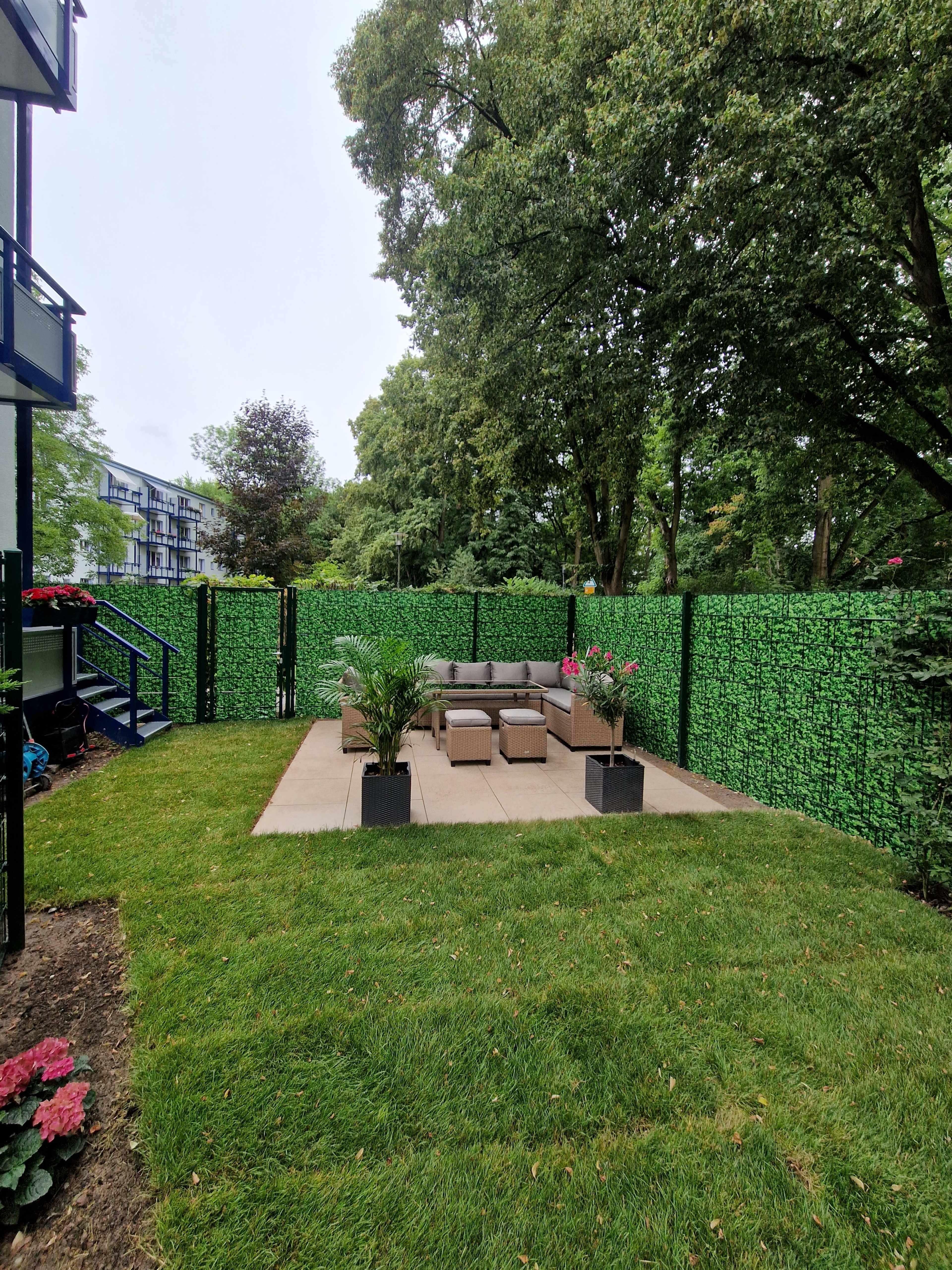 A landscaped backyard features a patio with seating surrounded by lush greenery and decorative plants.