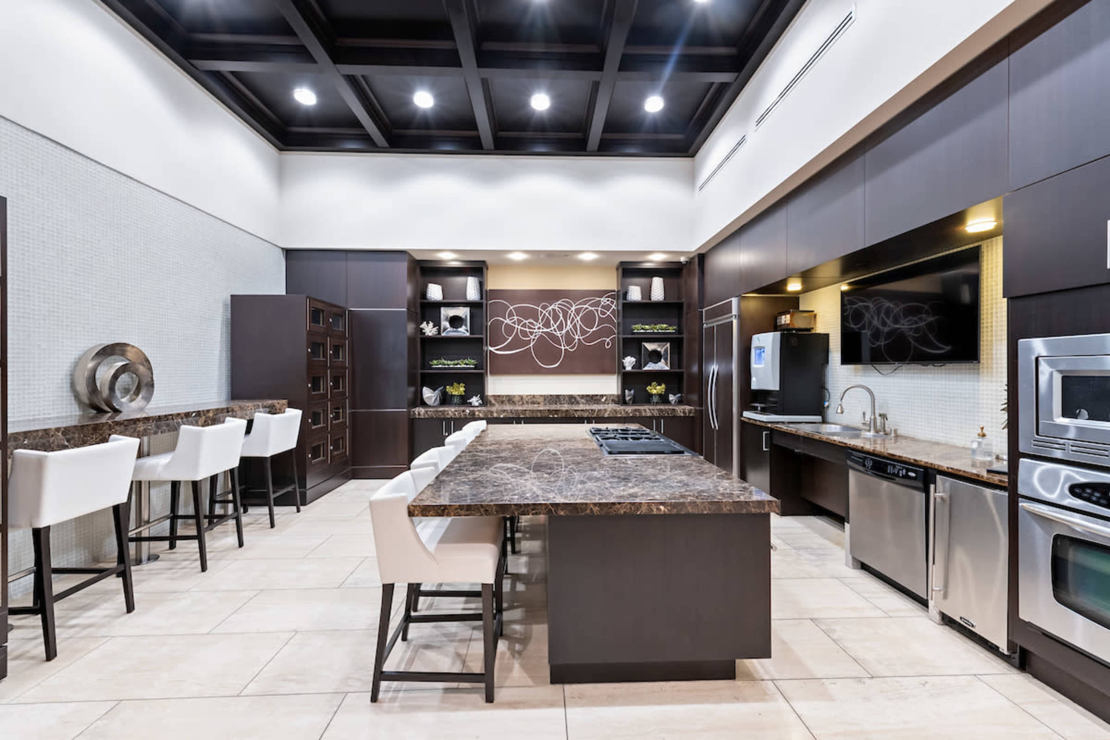 The image depicts a modern kitchen featuring dark cabinetry, a large island with a marble countertop, and bar seating.