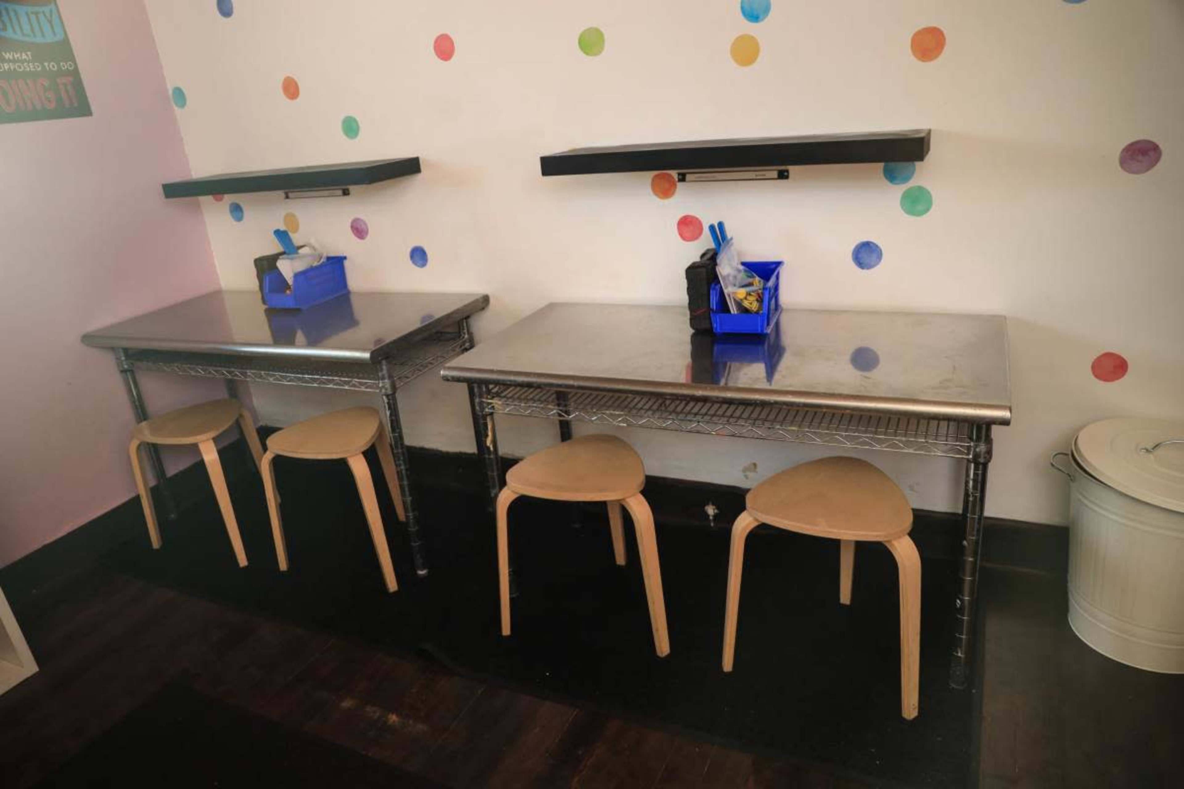 Two metal tables with wooden chairs sit against a wall decorated with colorful polka dots.