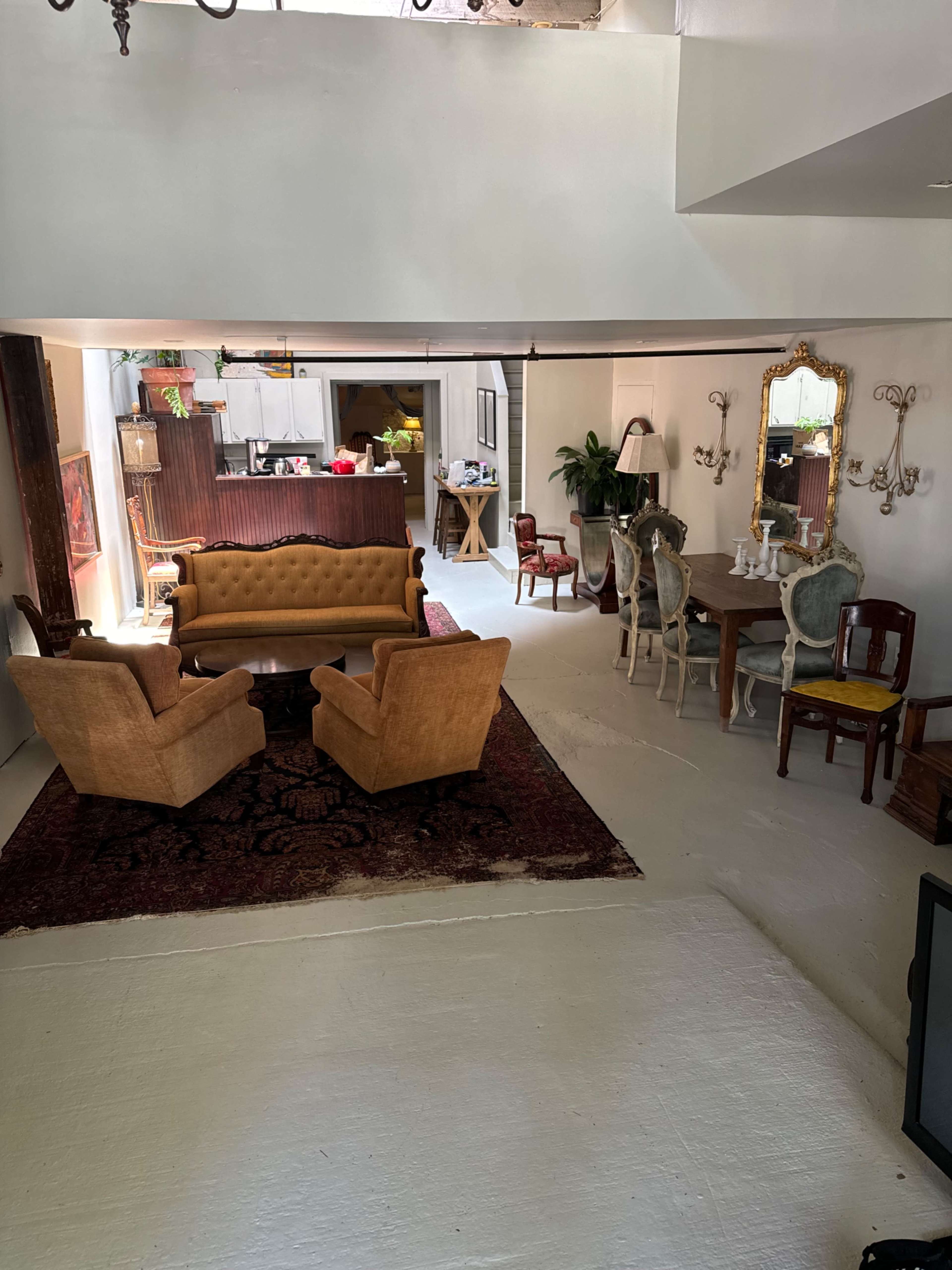 A spacious room with a seating area featuring two yellow armchairs, a brown rug, and a dining table with ornate chairs in a well-lit setting.