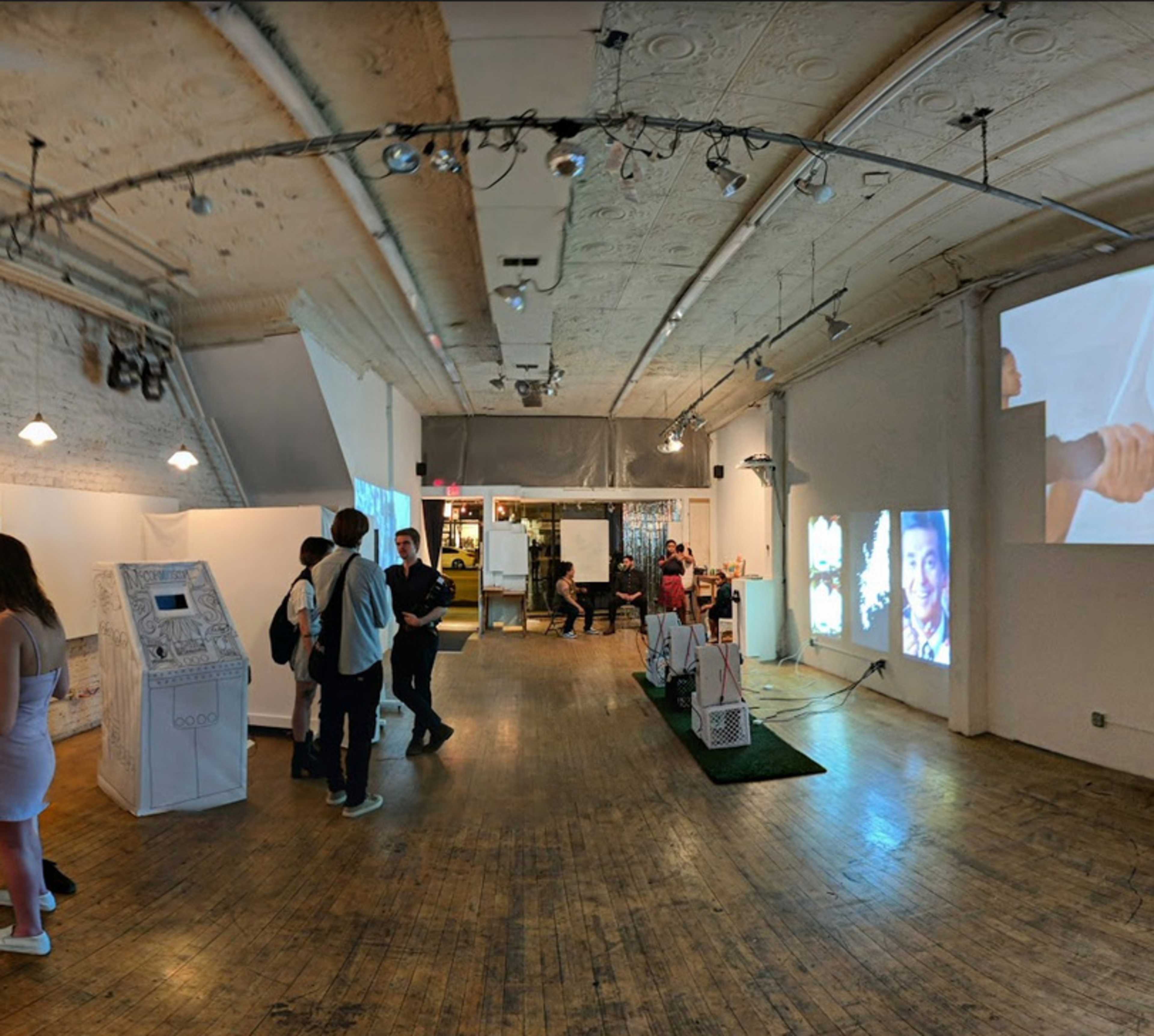 An art gallery with several people interacting, digital displays on the walls, and a kiosk at the front.