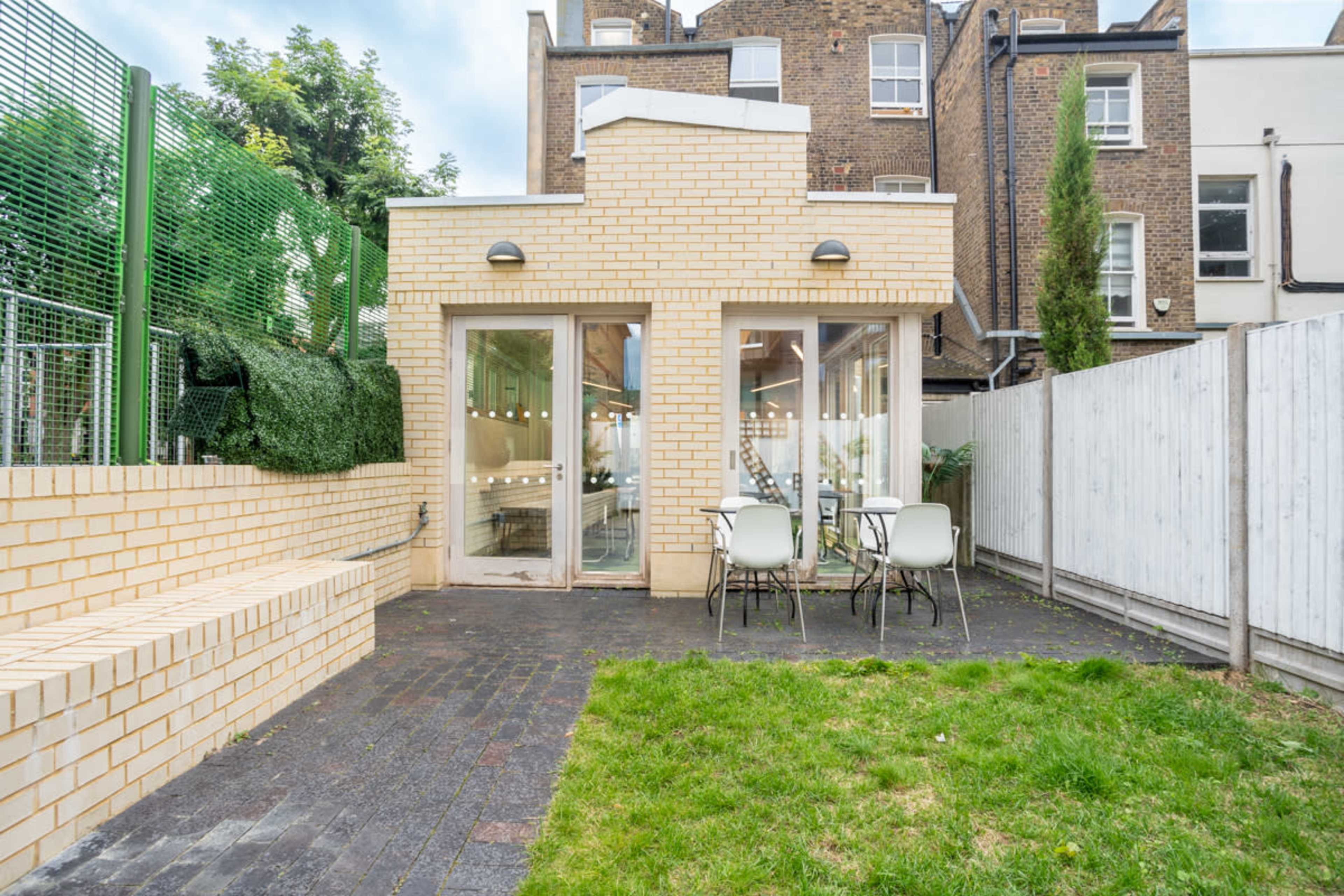 A modern brick extension features large glass doors opening to a small outdoor seating area with two chairs and a grassy space.