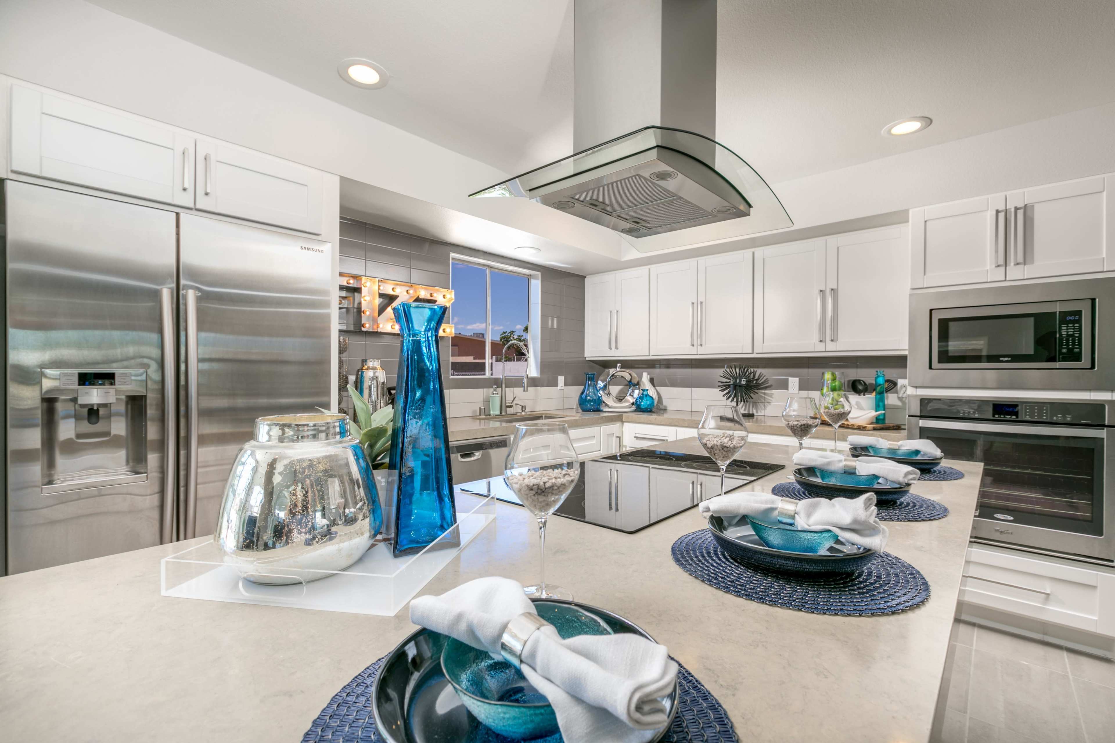 A modern kitchen with white cabinetry, stainless steel appliances, and a central island adorned with decorative glass vases and table settings.