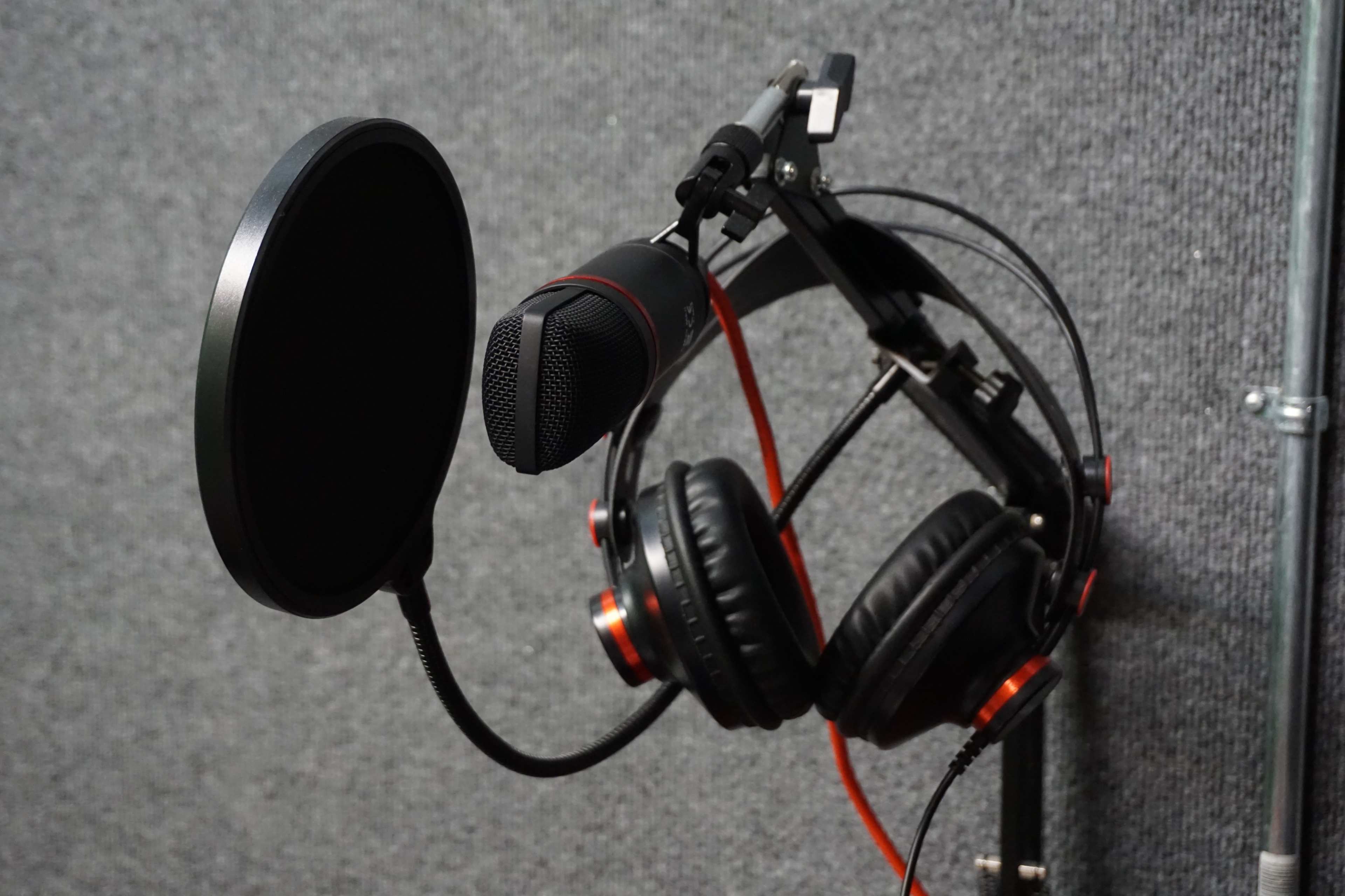 A microphone and a pair of headphones are mounted on a stand against a textured gray background.