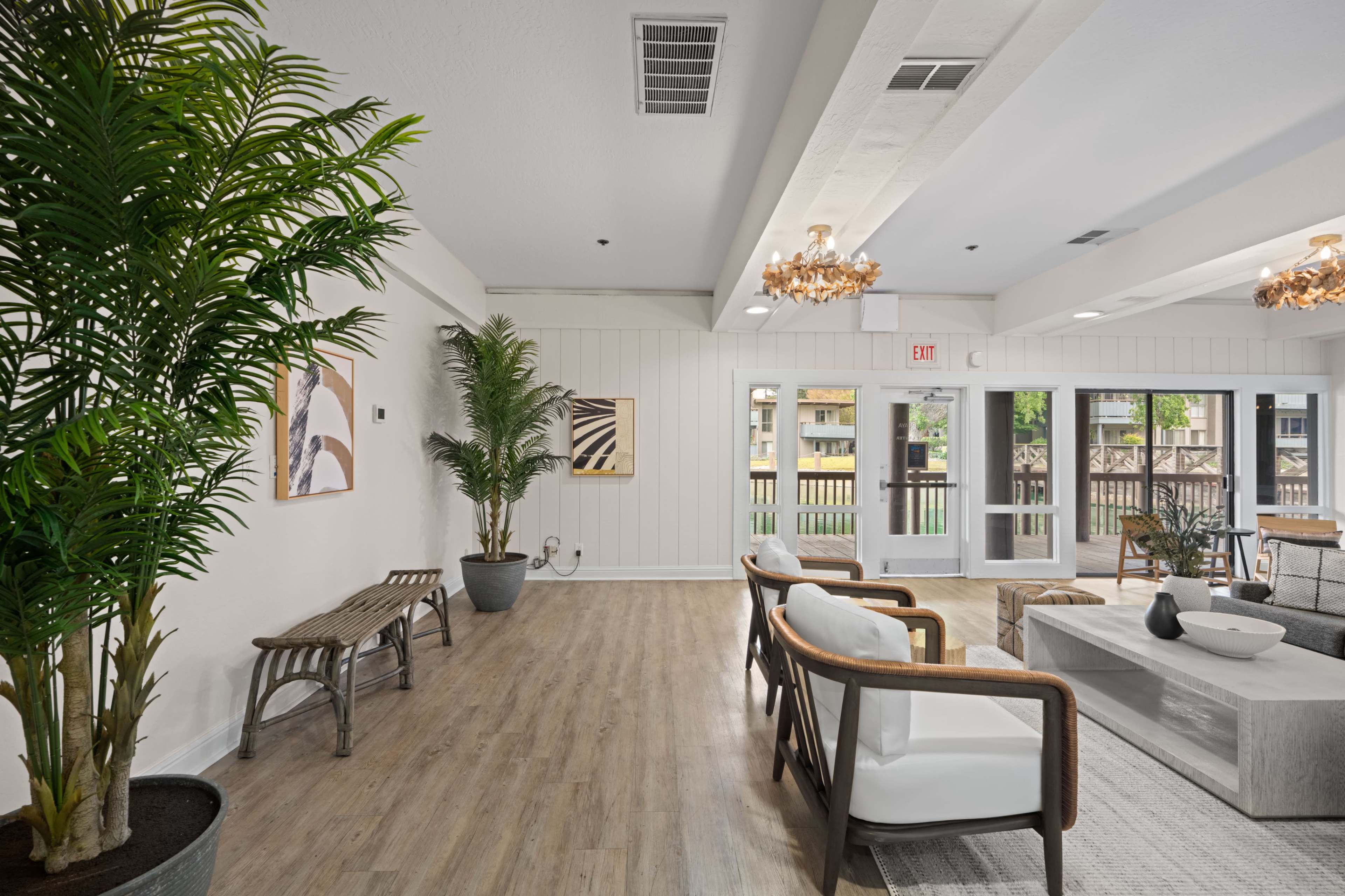 The image shows a modern lobby area with wooden flooring, large windows, comfortable seating, potted plants, and decorative lighting fixtures.