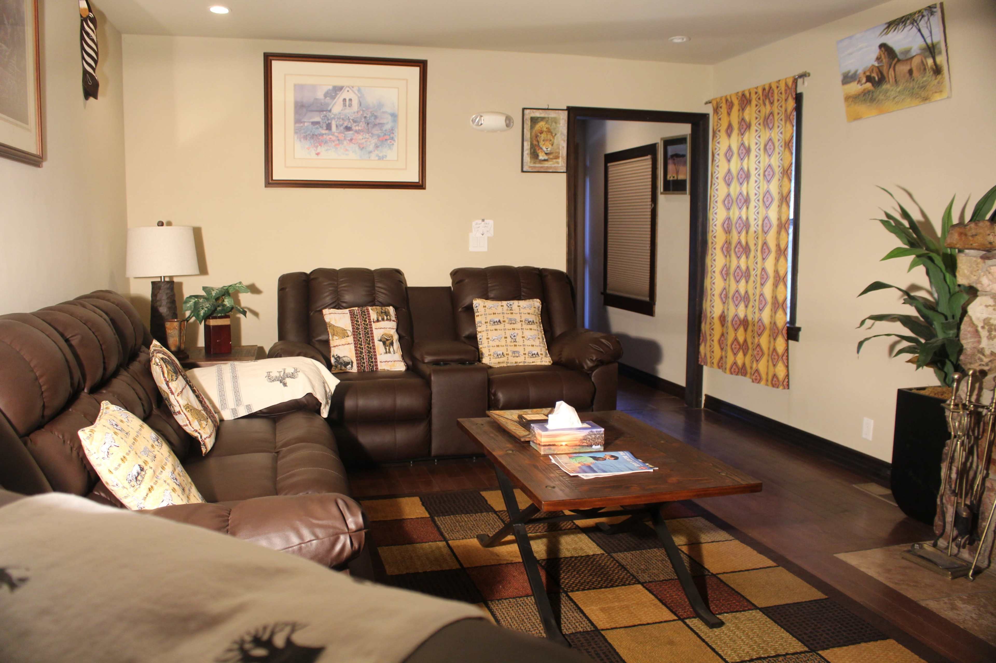 The image shows a cozy living room with brown leather sofas, a wooden coffee table, decorative pillows, and artwork on the walls.