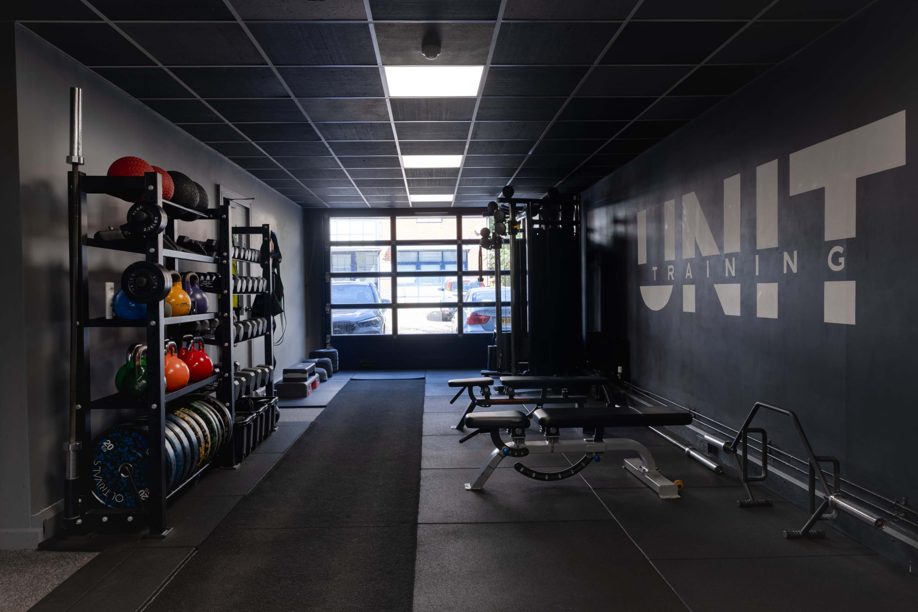 The image shows a fitness training area featuring exercise equipment, weights on racks, and a wall with the text "UNIT Training."