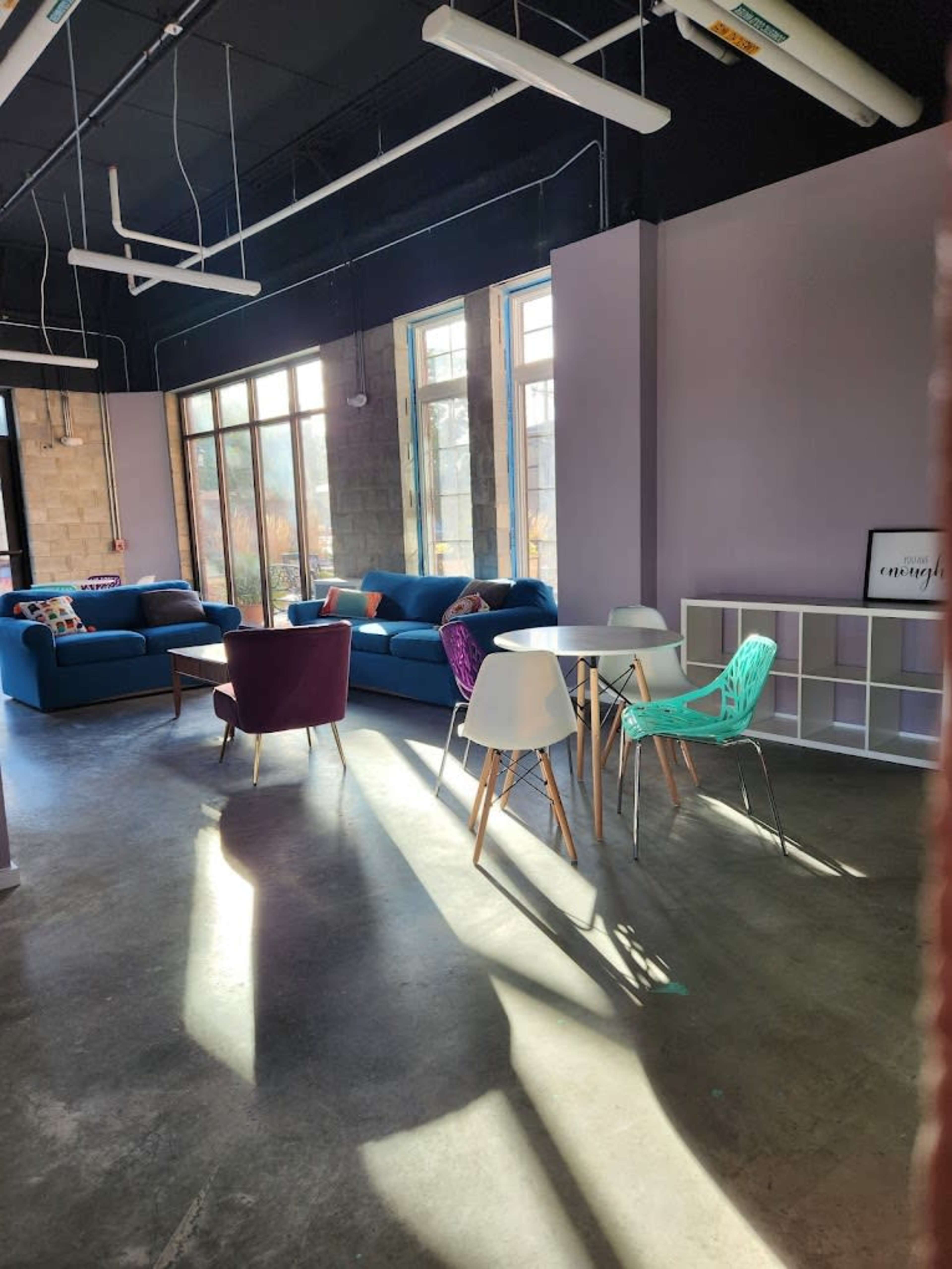 A modern, spacious lounge area with blue sofas, colorful chairs, and large windows allowing natural light to enter.