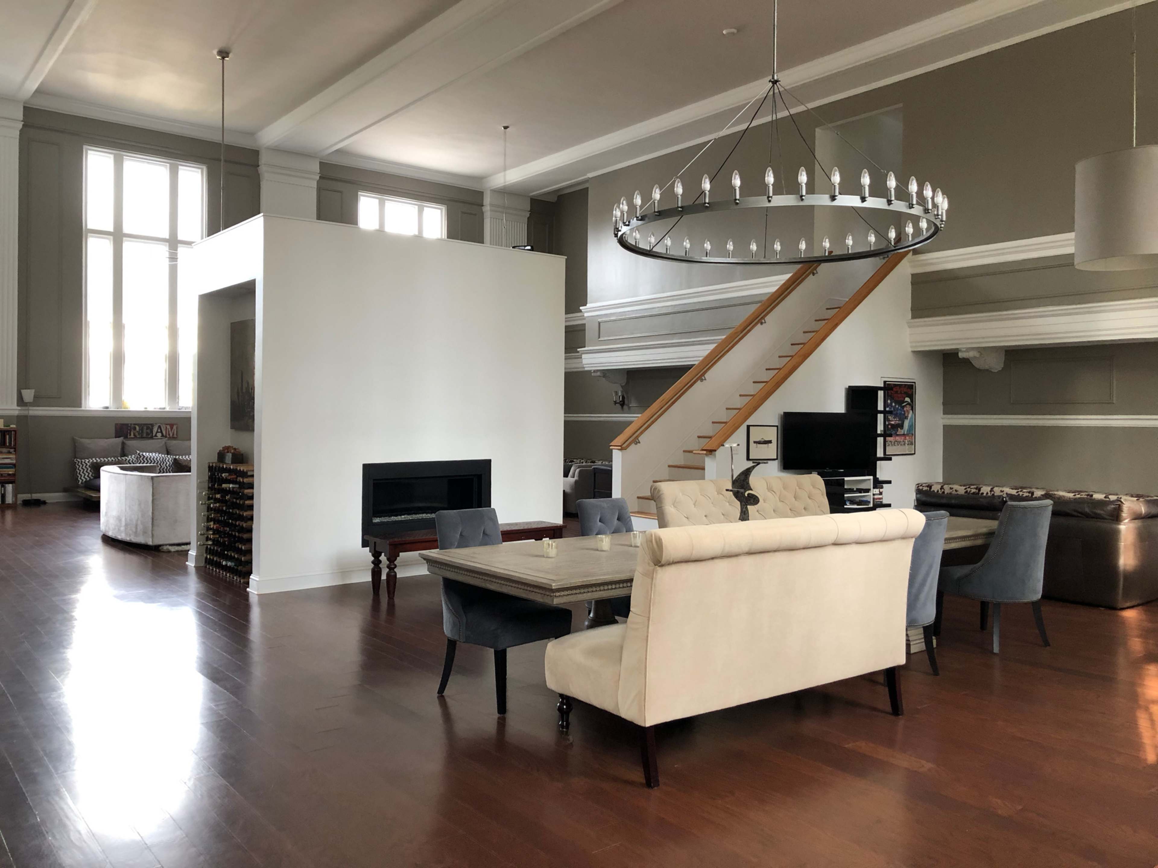 A spacious living area with a large chandelier, a staircase, a modern fireplace, and various seating areas.