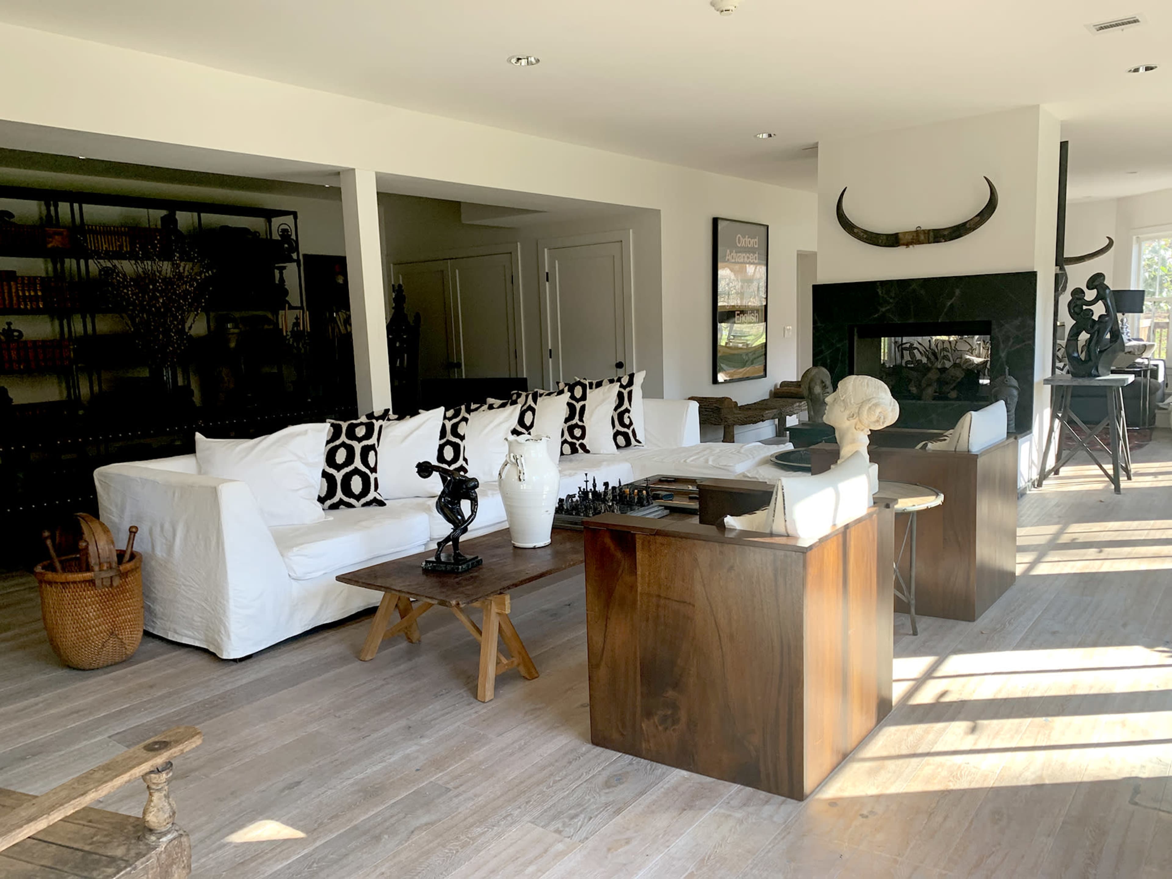 The image shows a modern living room with a white sofa, black and white patterned cushions, a wooden coffee table, and a fireplace, complemented by various decorative sculptures.