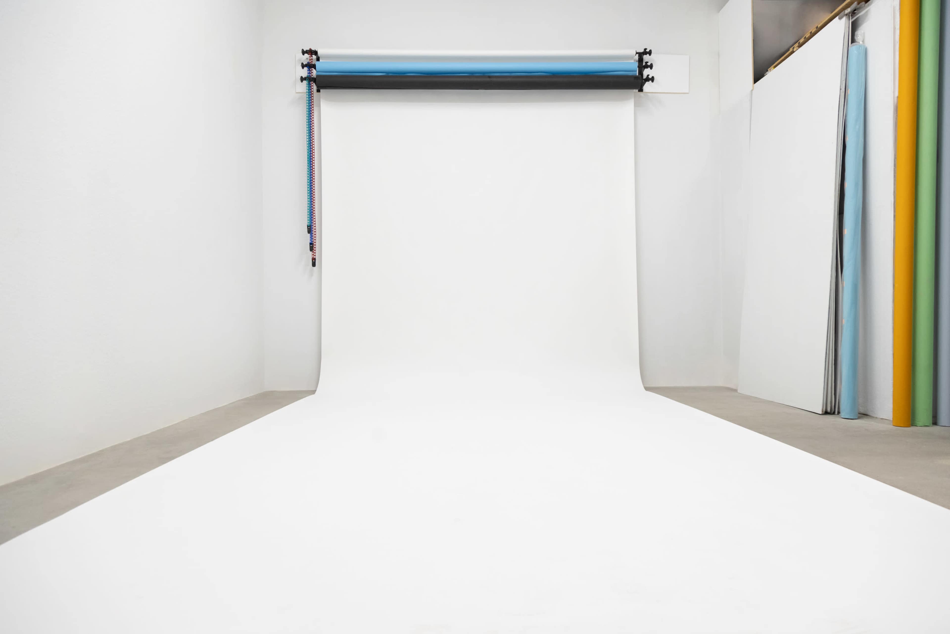 The image shows a photography studio with a white backdrop and various colored backdrops stored on the side.