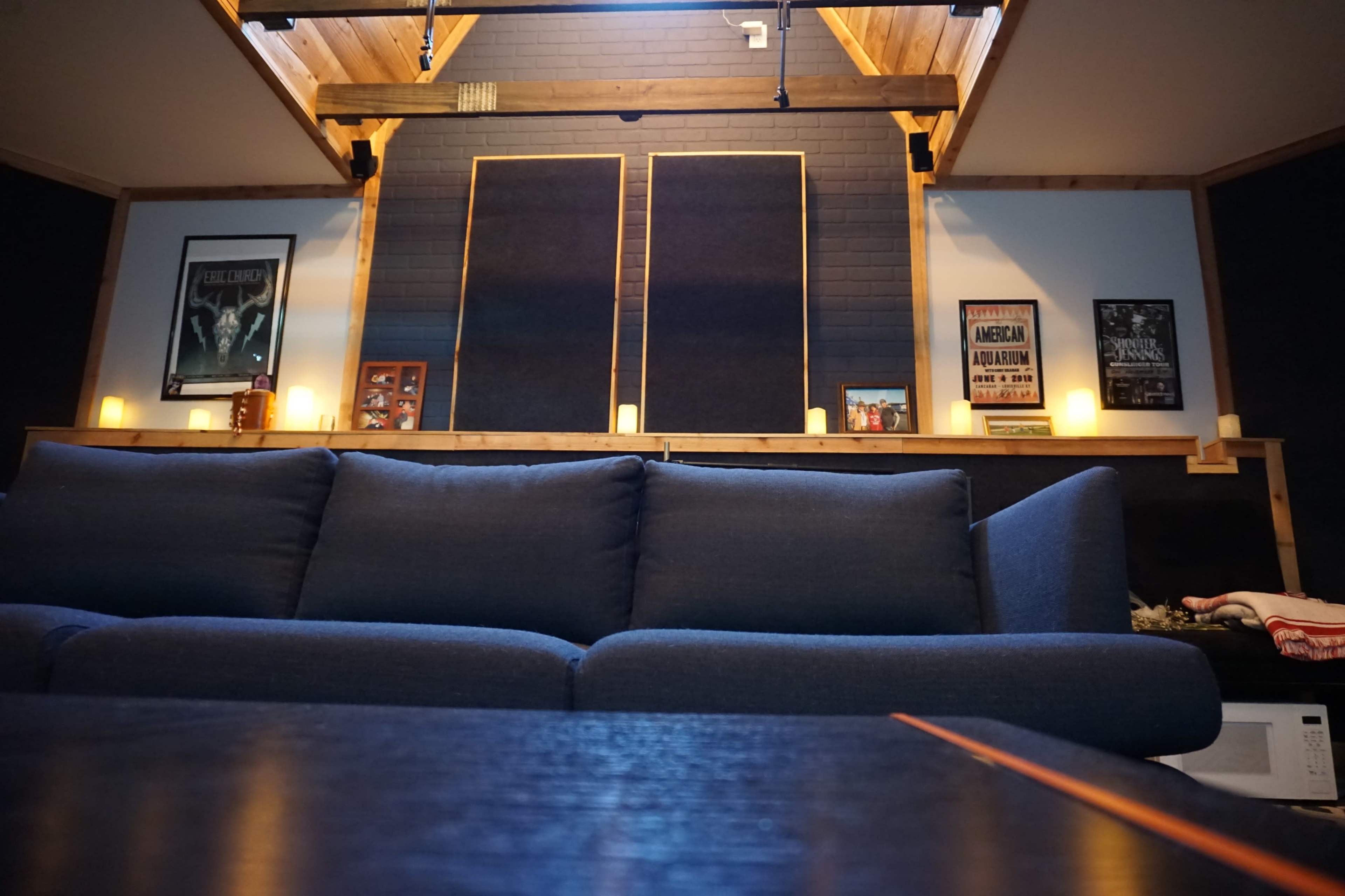 A cozy living room with a blue couch facing a wall adorned with framed posters and ambient candles.