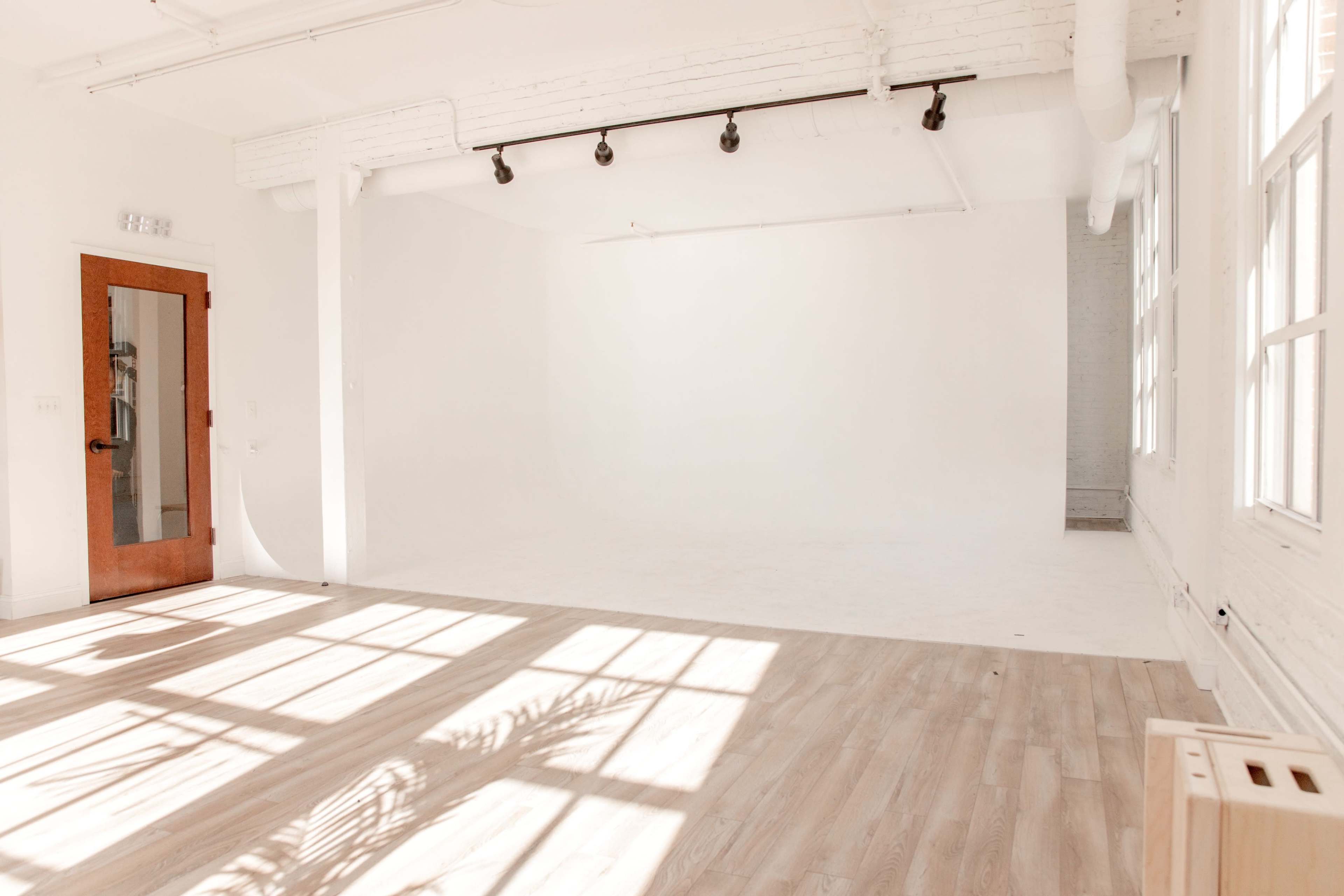 A bright, empty studio space with large windows and wooden flooring.