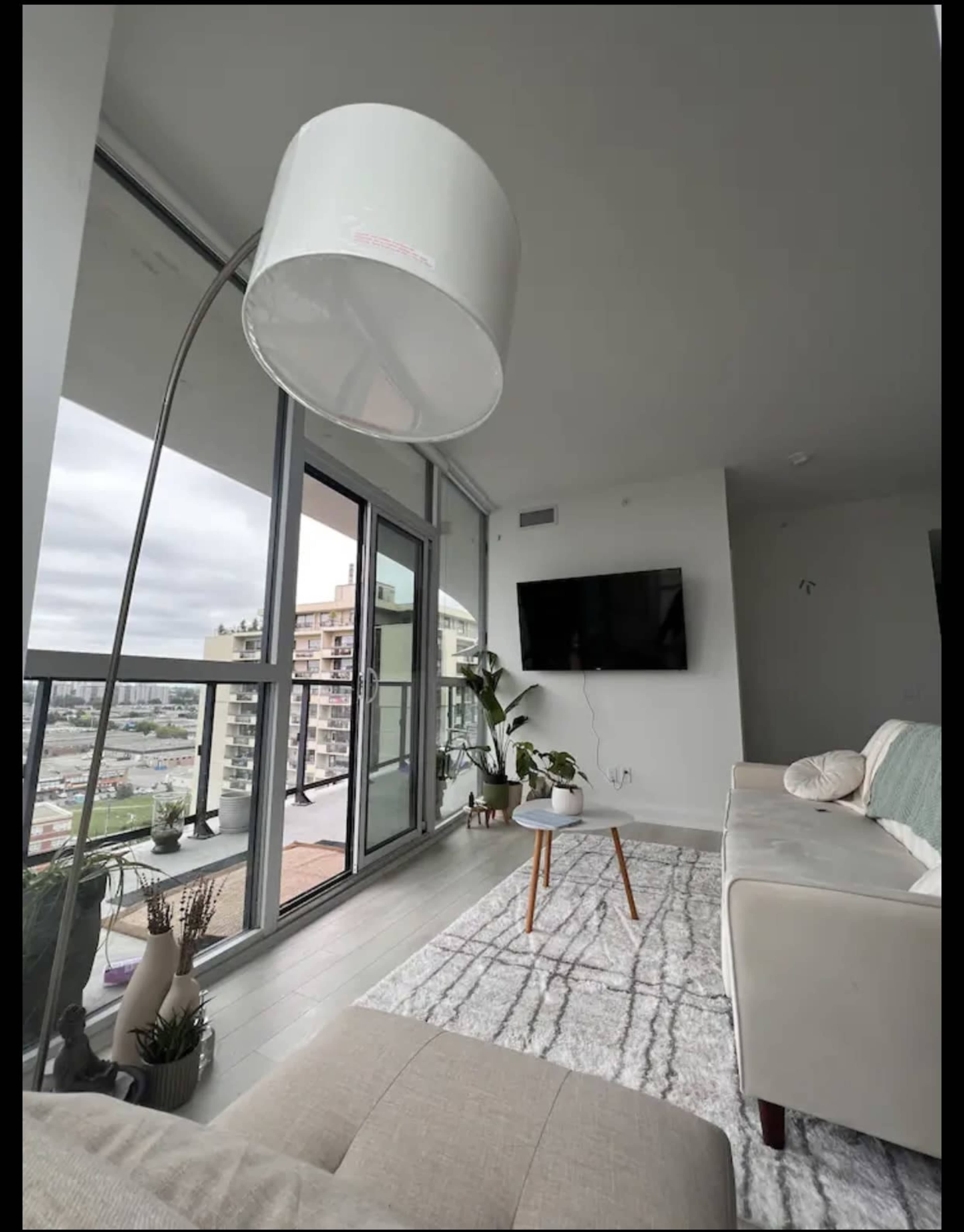 A modern living room with a large lamp, a sofa, a coffee table, and a view of the city through glass windows.