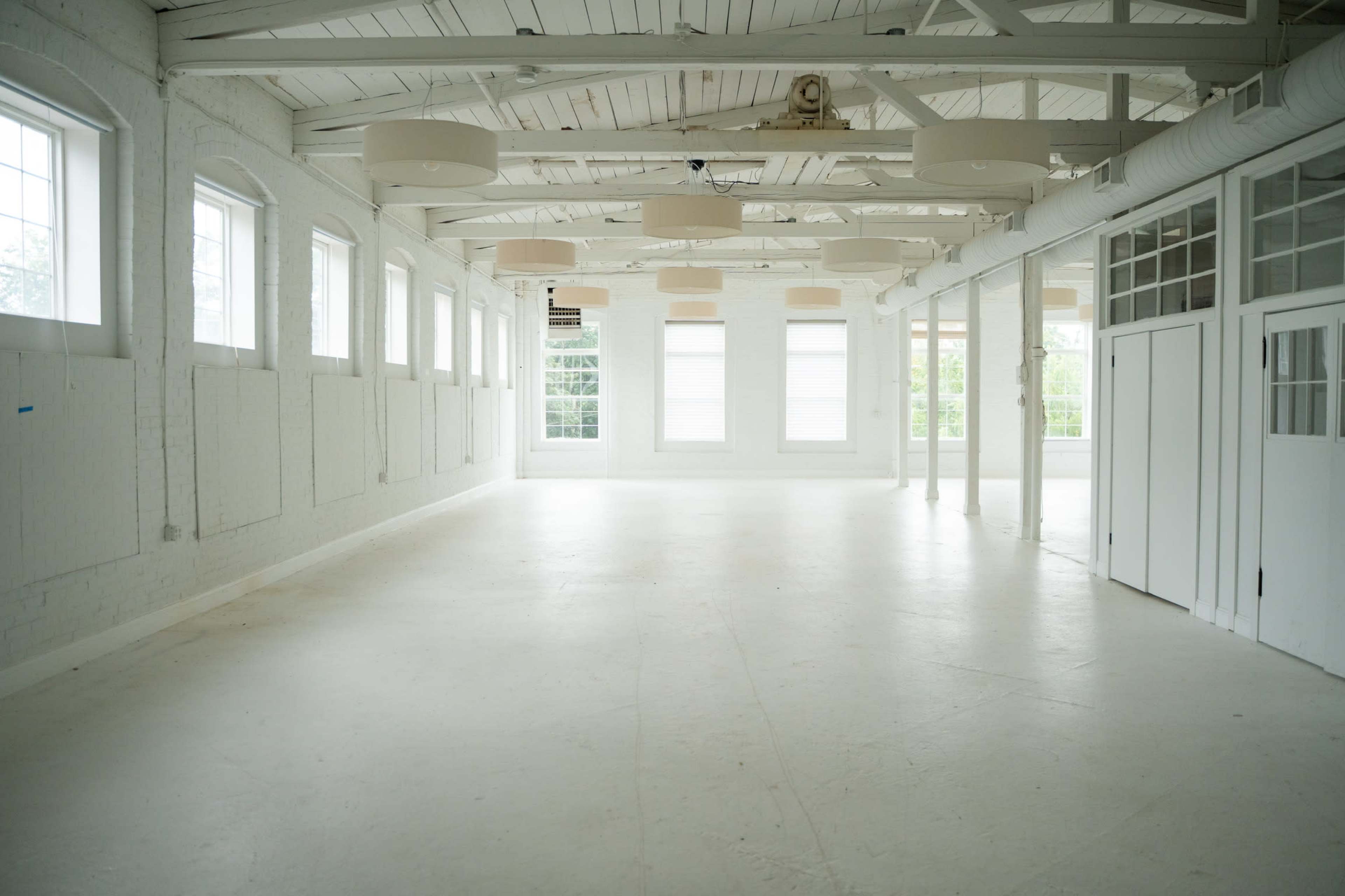 The image shows an empty, well-lit room with large windows and white walls and flooring.