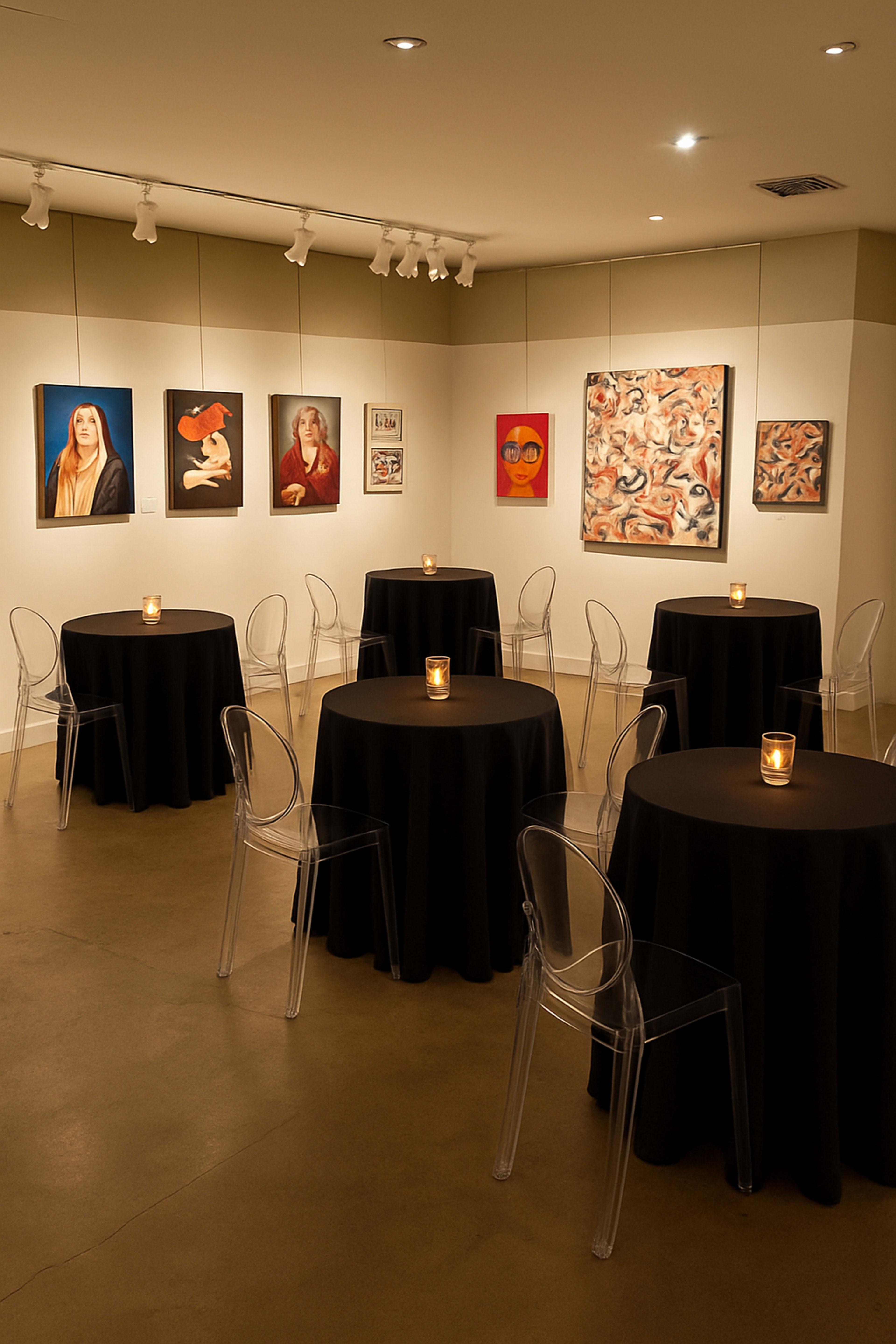 The image shows a well-lit gallery space with several round tables covered in black tablecloths, each with a candle, surrounded by various artworks displayed on the walls.